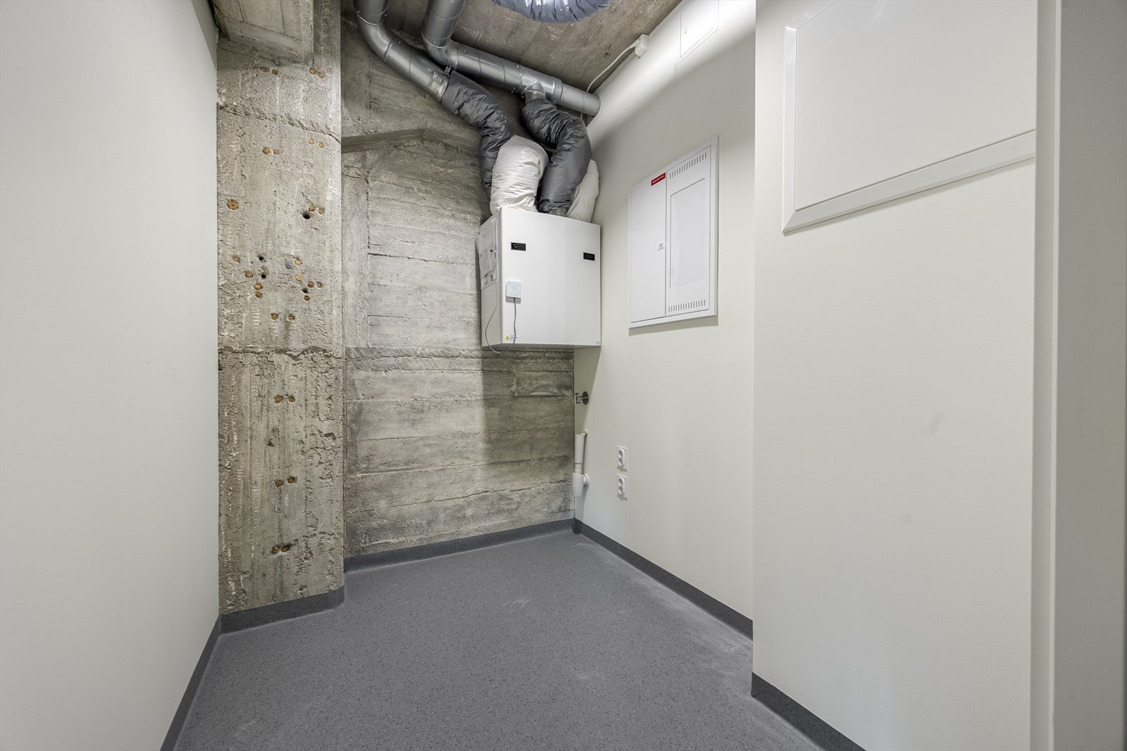 En praktisk, innvendig bod med leilighetens balanserte ventilasjonsanlegg, opplegg for vaskemaskin og sikrings- og vannskap. Gulvsluk. Galleribilde