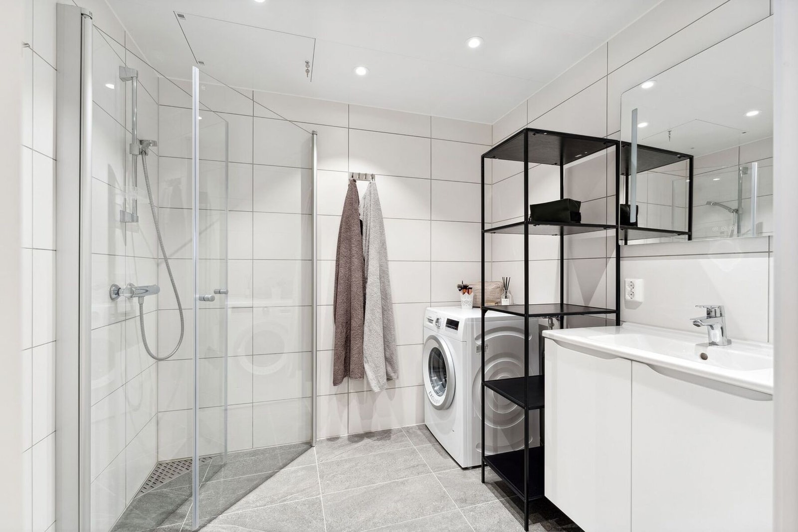 Badet er fra byggeår og fremstår delikat, med flislagte gulv og vegger samt behagelig gulvvarme. Badet er innredet med vegghengt toalett, dusjhjørne, stilren servantinnredning, samt opplegg for vaskemaskin. Galleribilde