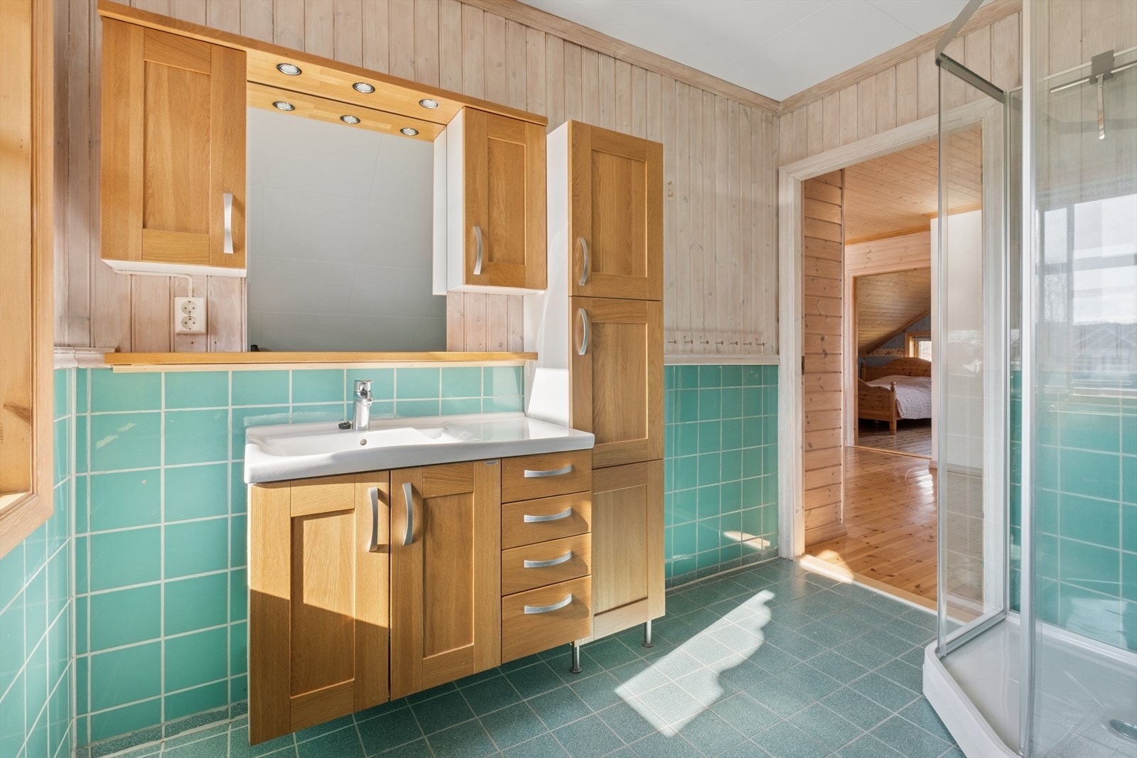 Badet på loftet er utstyrt med flislagt gulv med elektriske varmekabler, dusjkabinett og servant i innredning. Galleribilde