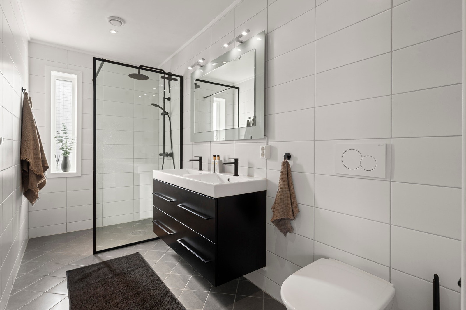 Boligen har to delikate bad, ett i hver etasje, som gir en praktisk og familievennlig løsning i hverdagen. Badet i 2. etasje fremstår moderne og stilrent med flislagte overflater, dusjnisje, vegghengt toalett og dobbel servant med god oppbevaringsplass. Galleribilde