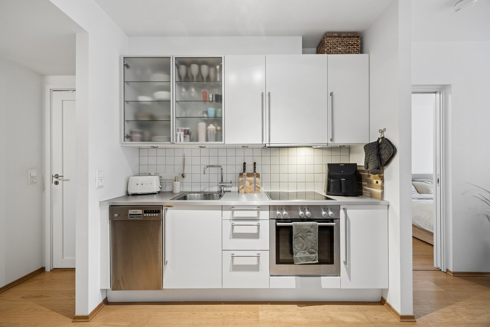 Kjøkkeninnredning med hvite, glatte fronter og benkeplate i grå laminat. Integrert stekeovn, keramisk koketopp og oppvaskmaskin. Galleribilde