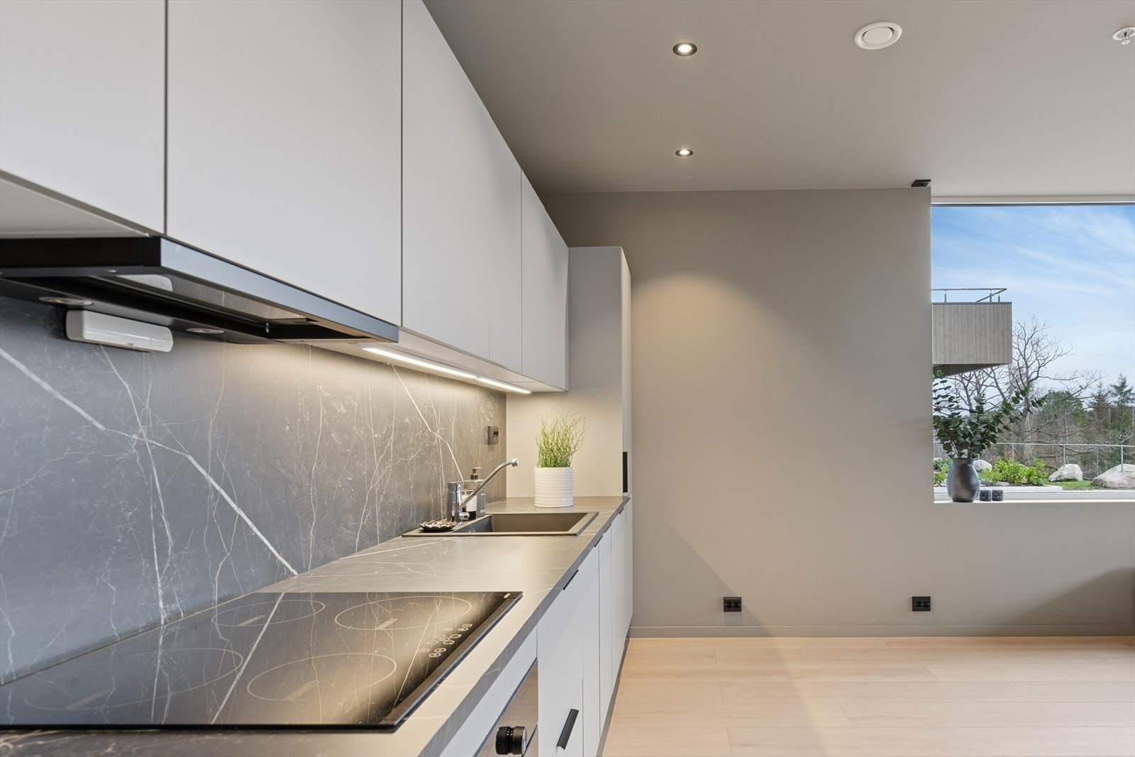 Kjøkken har innredning med hvite glatte fronter og laminat benkeplate som er trukket som backsplash for et stilrent uttrykk. Galleribilde