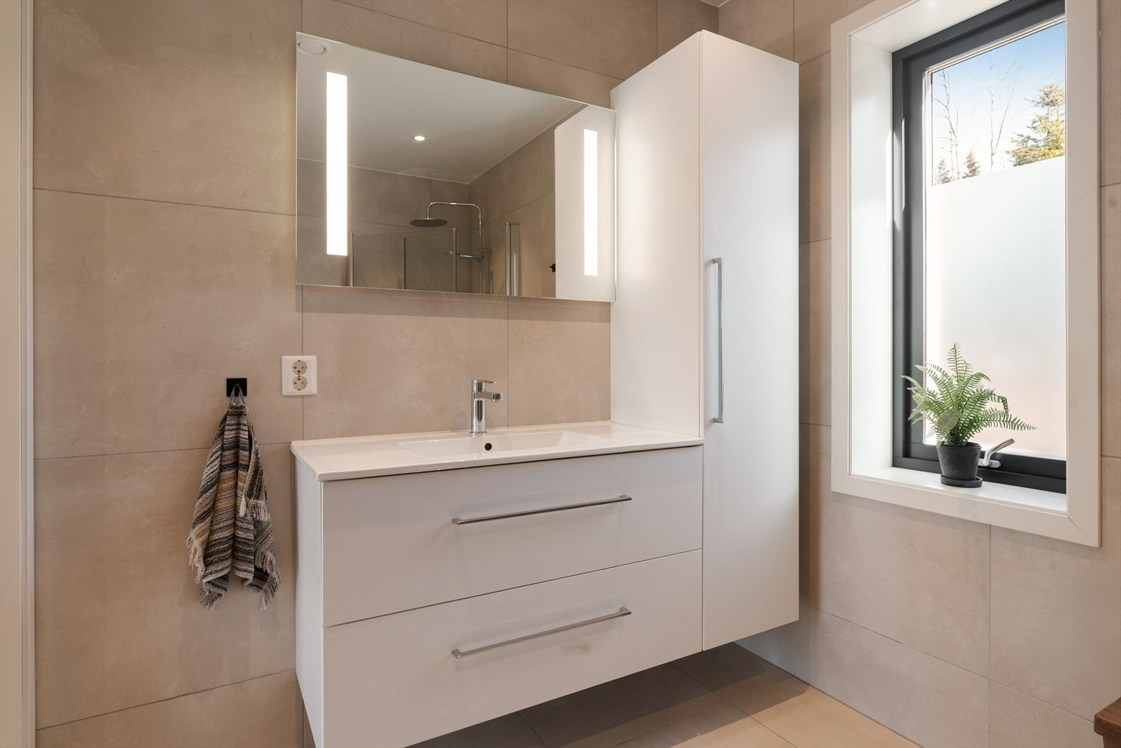 Badet inneholder heldekkende servant med underskap, høyskap, speil med lys, vegghengt toalett og dusjhjørne med regndusj. Galleribilde