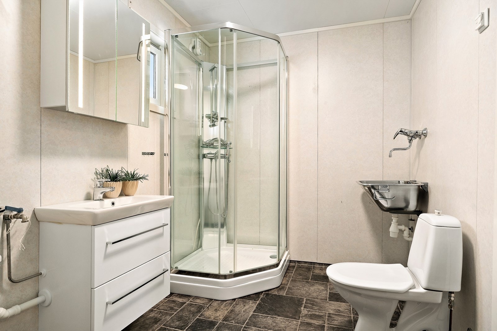 Badet har innredning med nedfelt vask, dusjkabinett og opplagt vann og avløp til vaskemaskin, samt stål skyllekar. Galleribilde