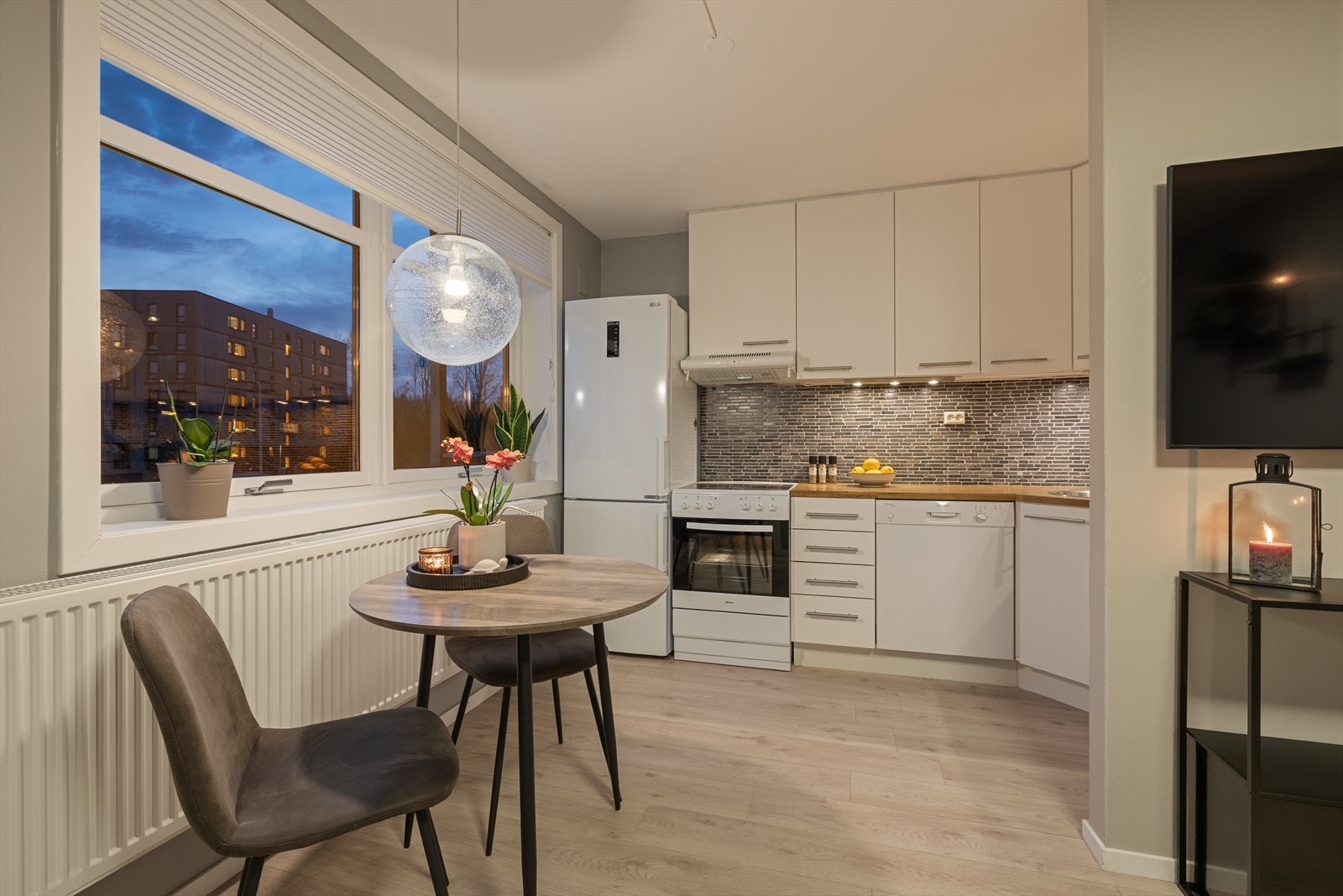 Kveldstemning. Kjøkkeninnredningen har lyse, slette fronter og laminert benkeplate. Rommet varmes opp av en ny vannbåren radiator fra 2022. Galleribilde