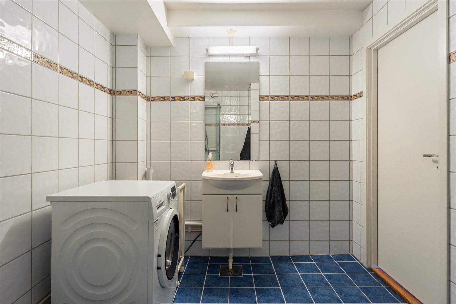 Lys og pen baderomsinnredning med underskap, servant og speil med belysning over. Galleribilde