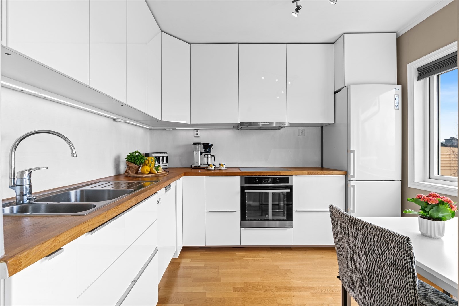 Kjøkkeninnredning fra IKEA (2015) med et moderne uttrykk, bestående av glatte, folierte høyglansfronter og heltre benkeplate med nedfelt kum i rustfritt stål. Belysning under overskapene gir gode arbeidsforhold. Galleribilde