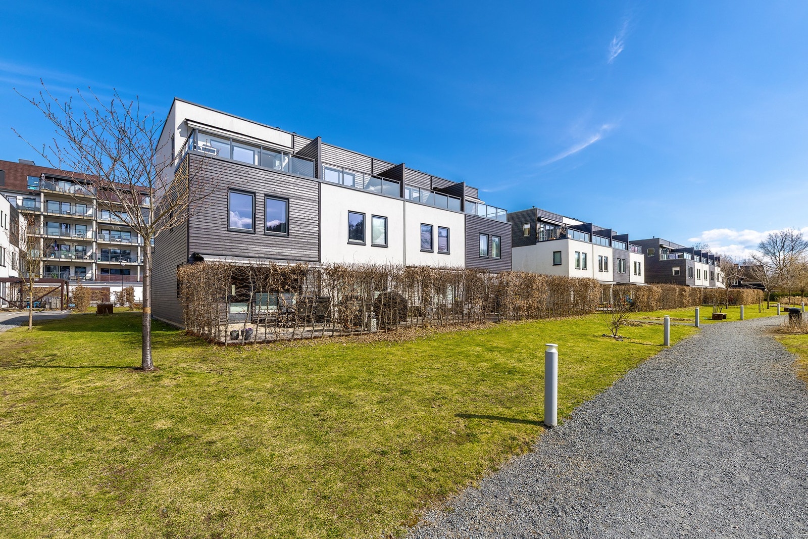 Moderne enderekkehus i tre etasjer med store vinduer og private terrasser, omringet av grøntområder og gangstier. Galleribilde