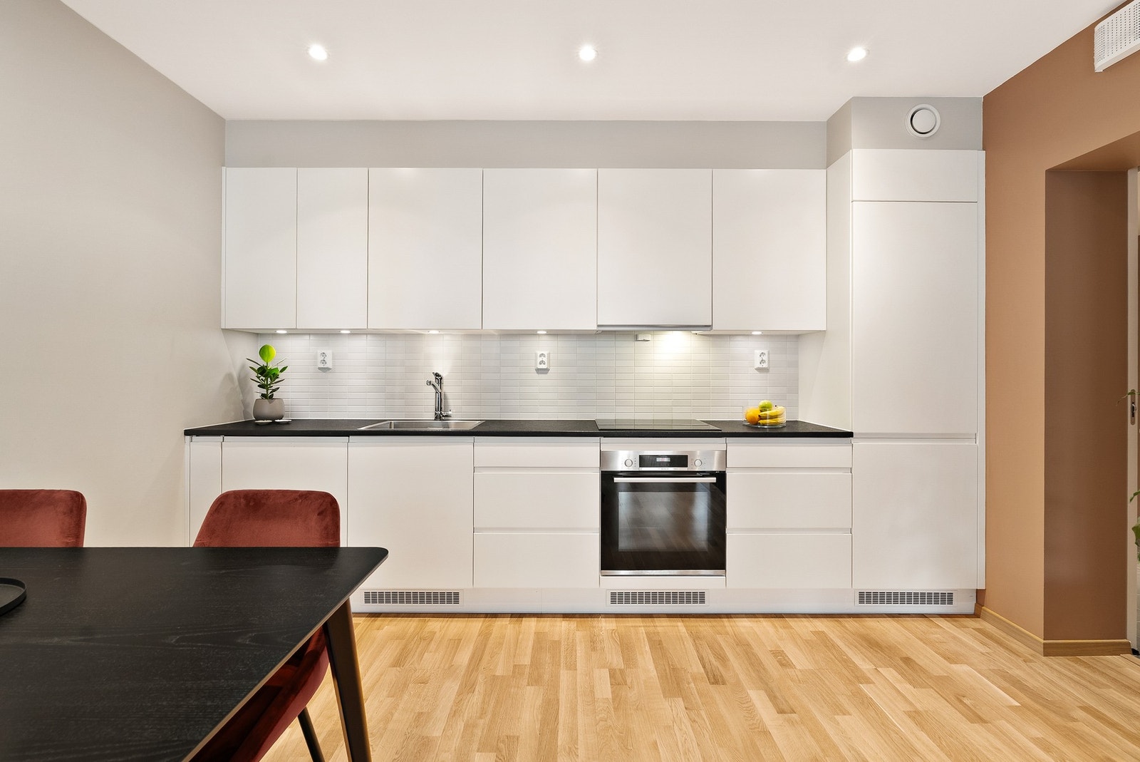 Pent og tidløst kjøkken med hvite slette fronter og benkeplate av laminat. Fliser på vegg over benk. Downlights under overskap. Galleribilde