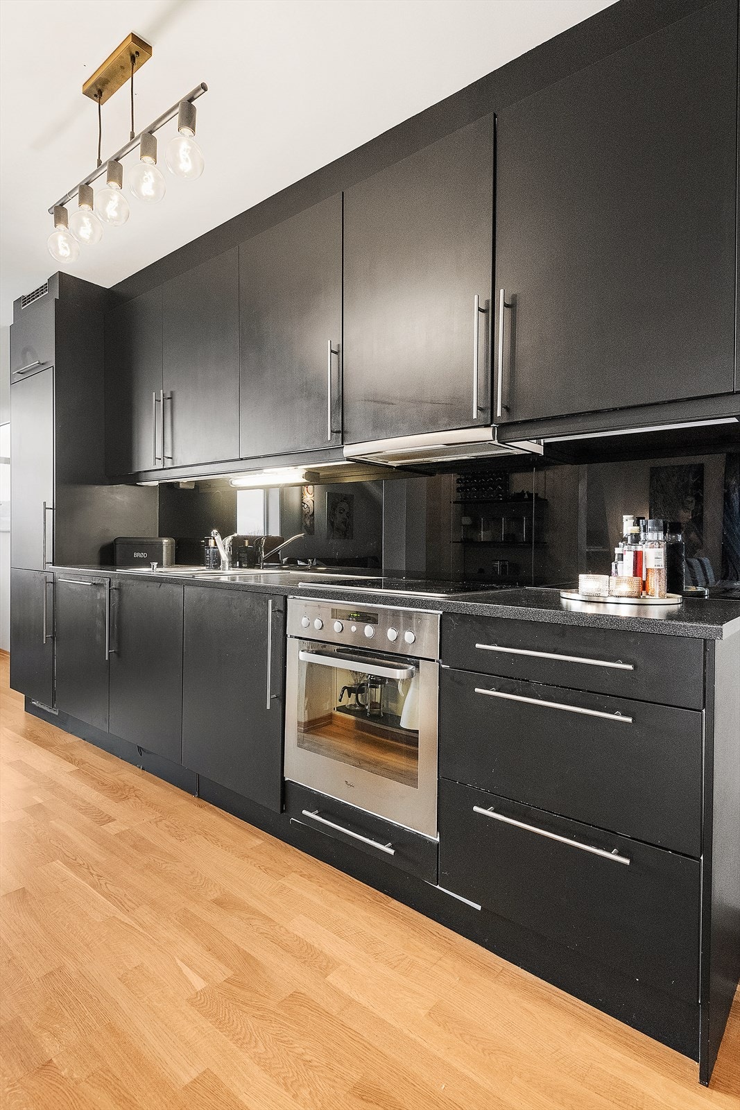Kjøkkenet har en enkel innredning med moderne uttrykk. Denne har av dagens eier blitt frisket opp med en mørk farge for å komplimentere boligens ellers moderne uttrykk. Galleribilde
