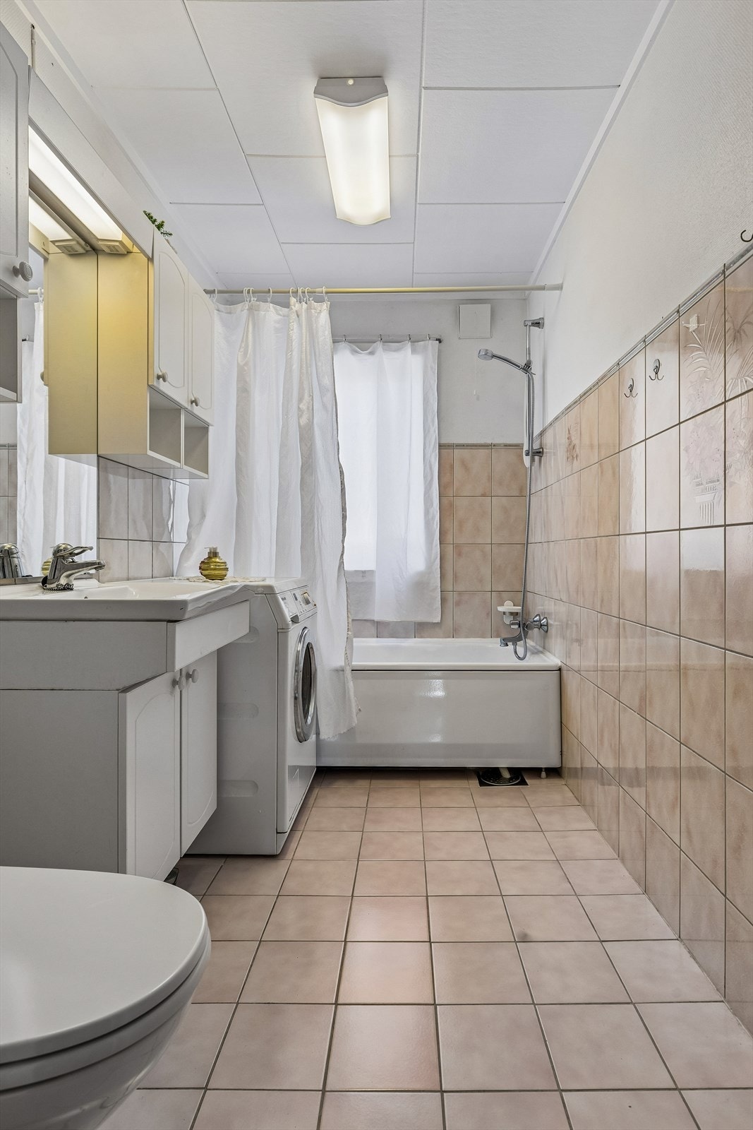 Badet har flislagt gulv med elektriske varmekabler, badekar med dusj og opplegg for vaskemaskin. Galleribilde