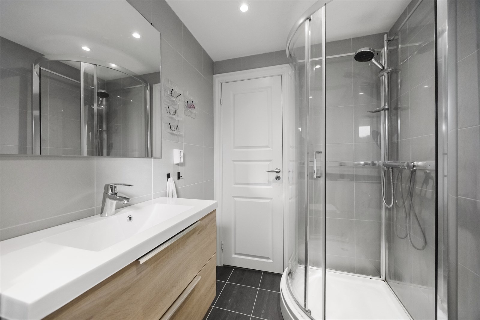 Baderom med overflater bestående av flislagt gulv med elektriske varmekabler, flislagte vegger og panel i taket. Badet har slett innredning med skuffer og heldekkende servant. Galleribilde