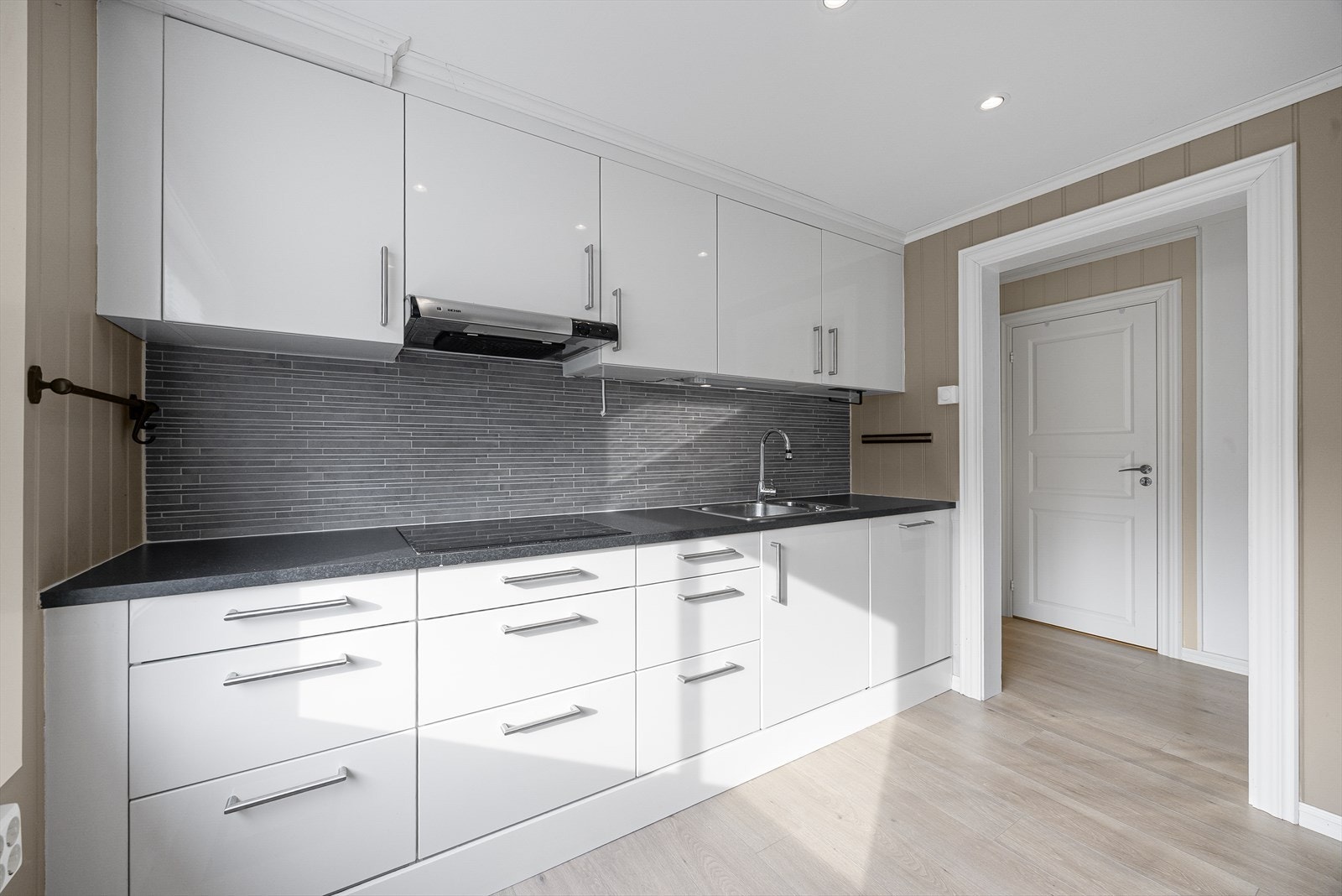 Takhøy kjøkkeninnredning fra HTH med slette fronter og laminert benkeplate. Kjøkkenet er utstyrt med integrerte hvitevarer som oppvaskmaskin, kjøleskap/frys, stekeovn samt nedfelt koketopp (induction) Galleribilde