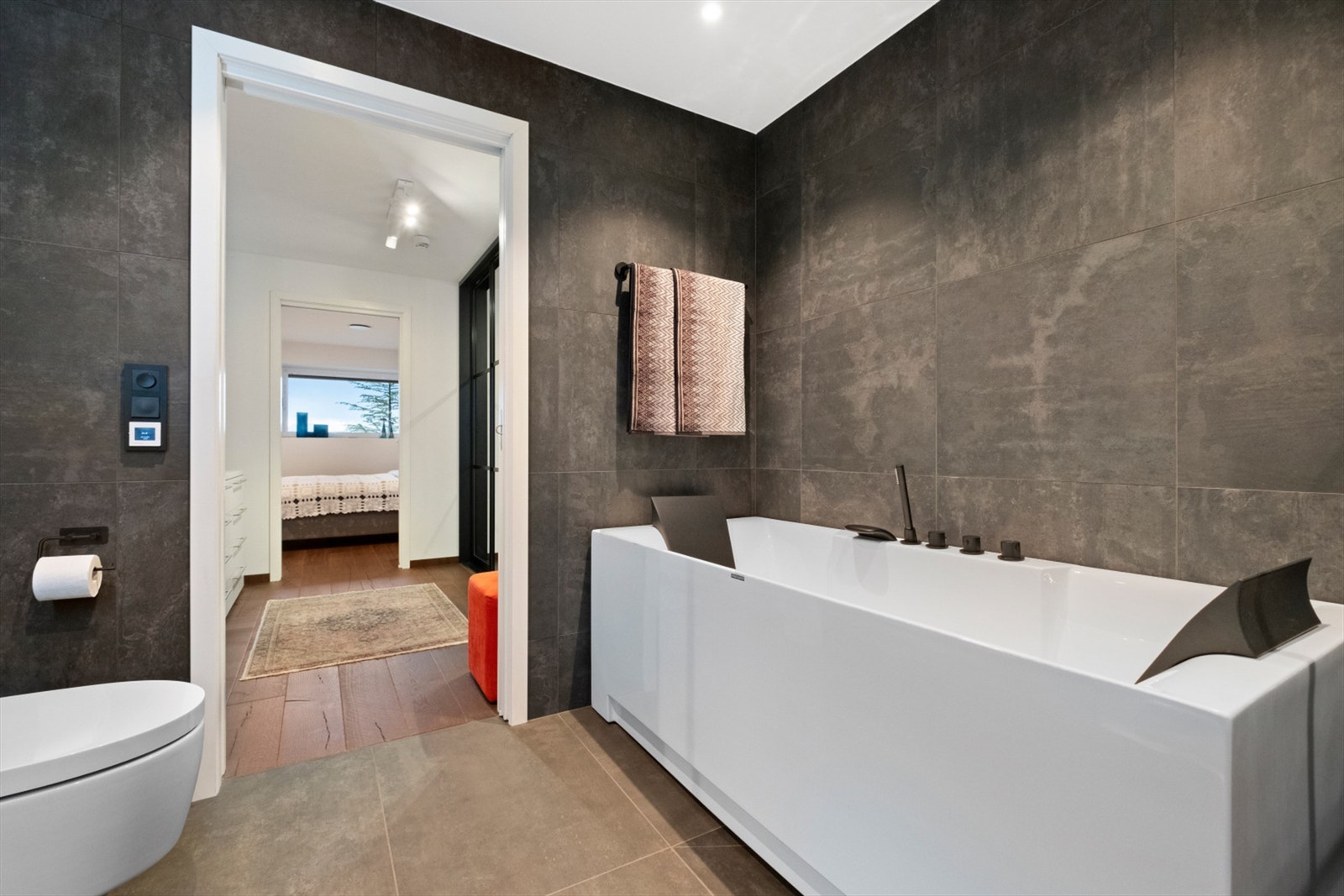 Badet har frittstående badekar med innfelt badekarsarmatur i tillegg til dusjhjørne med glassvegger og vegghengt dusjarmatur med hånddusj og regndusj Galleribilde