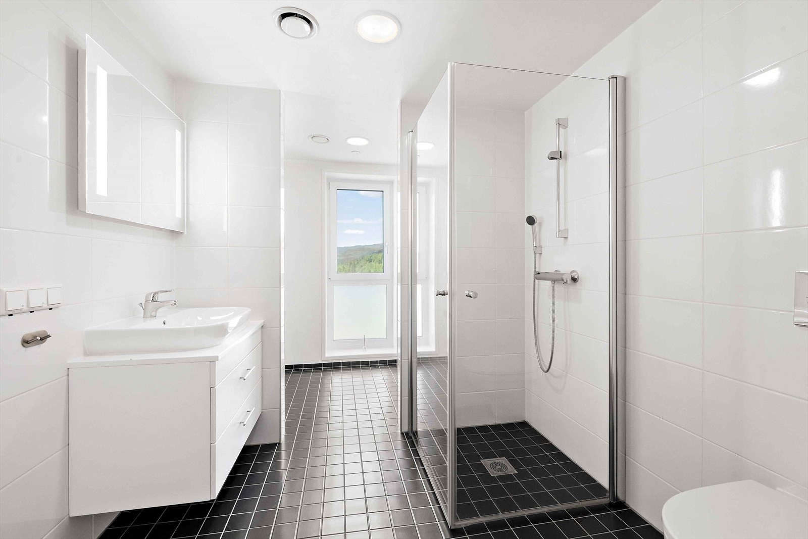 Badet er stort og praktisk utformet med to soner en for bad og en for vaskerom. Veggene og gulvet er flislagt, og gulvet har varmekabler for en lun start og slutt på dagen. Galleribilde