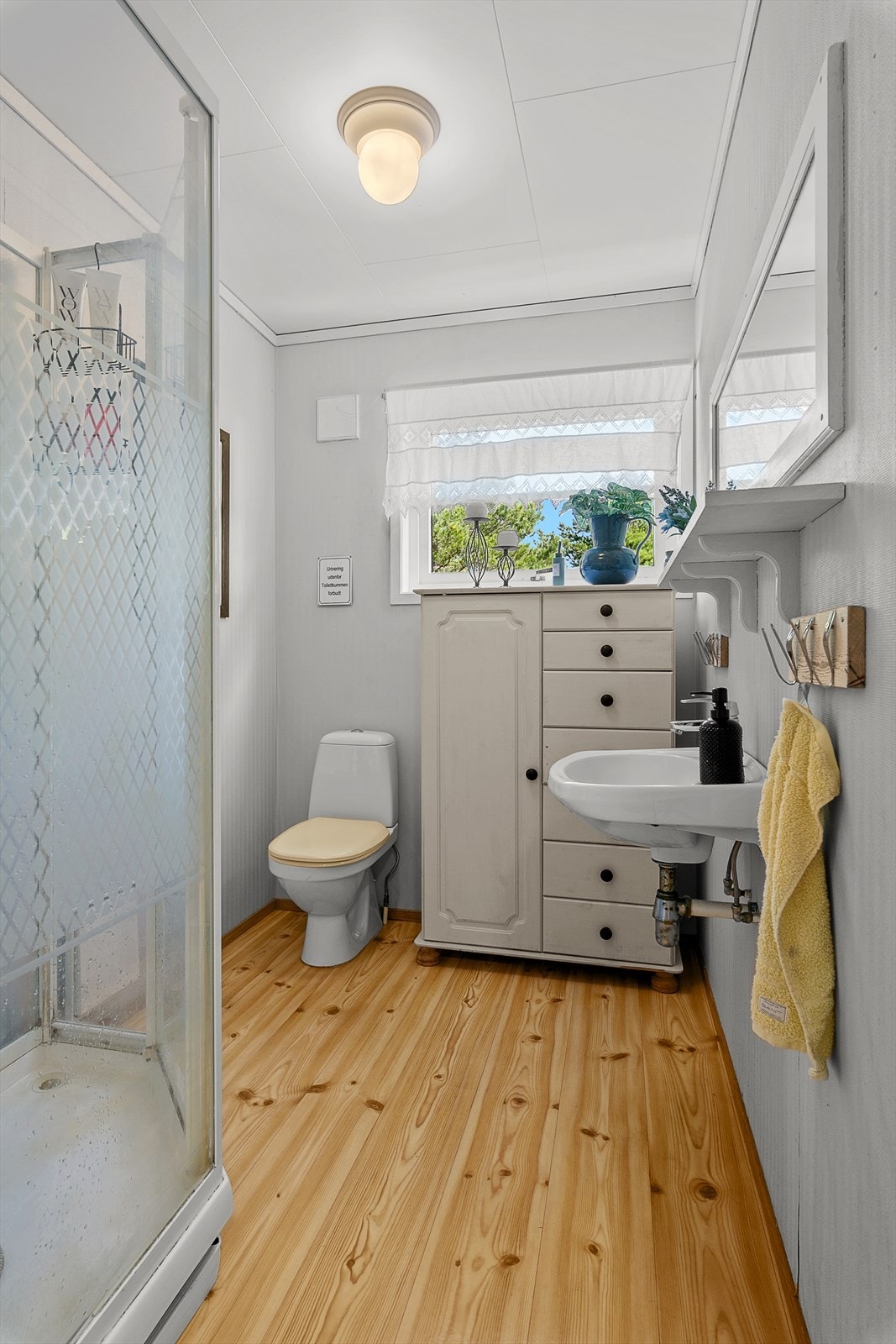 Badet i 1. etg. har belegg på gulv og tapet på vegger. Rommet inneholder wc, dusjkabinett og servant. Galleribilde