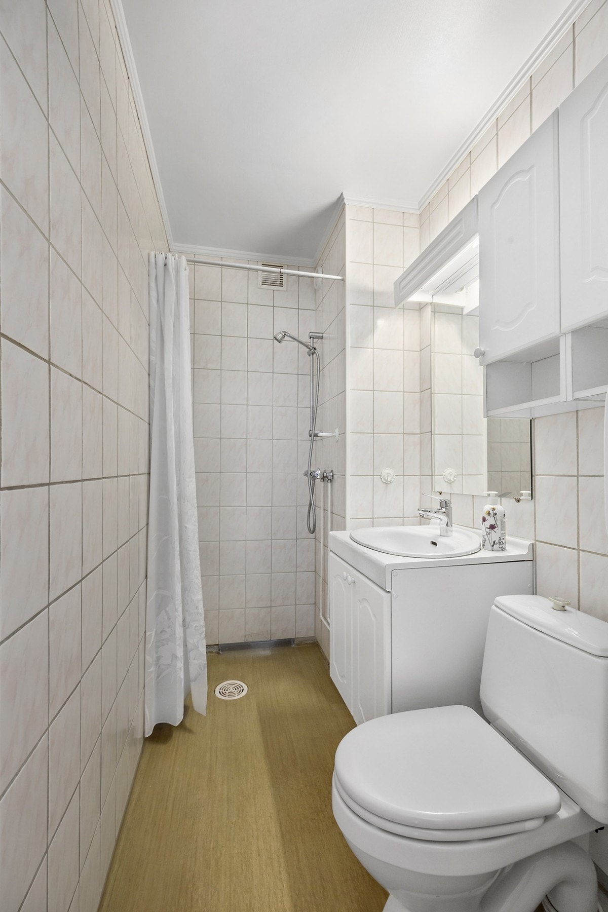 Bad 2 med fliser på vegg innredet med WC, servantinnredning med tilhørende speil samt dusj. Galleribilde