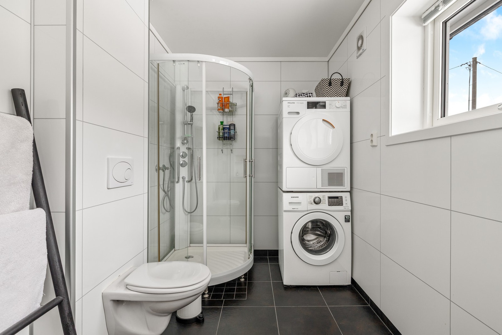 Badet ligger fint til utenfor soverommene, innredet med store, sorte gulvfliser og hvite våtromsplater i flismønster. Galleribilde