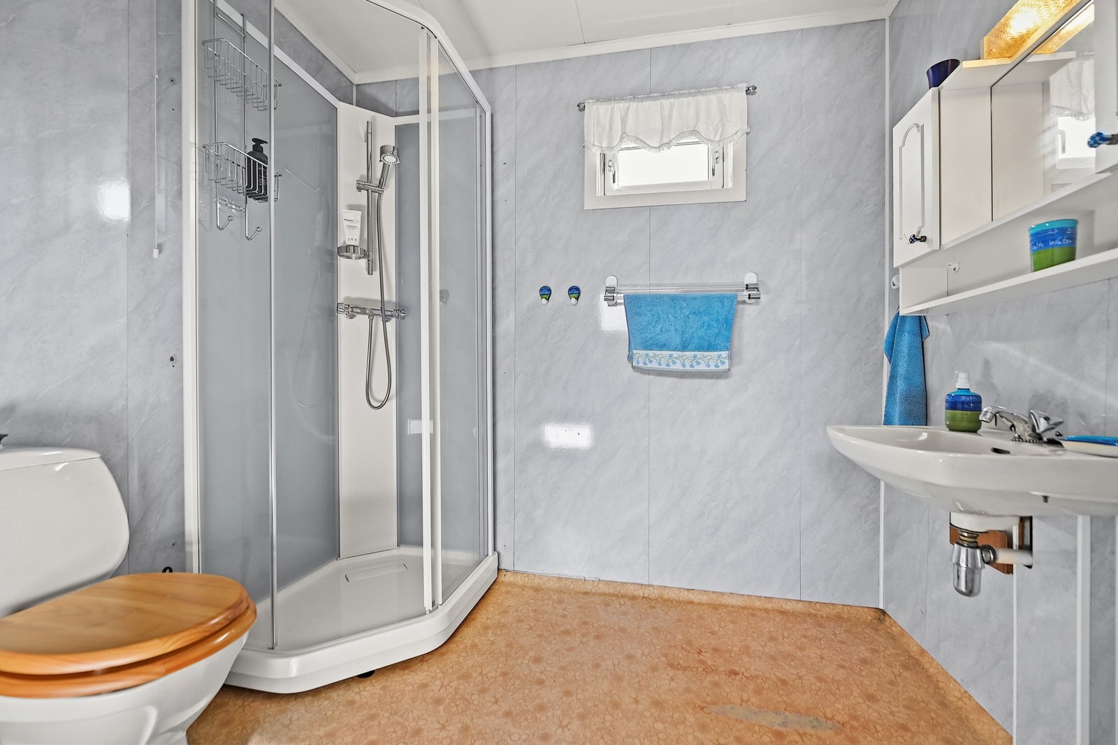 Badet er innredet med gulvstående wc, servant, speil, sideskap og dusjkabinett. Galleribilde