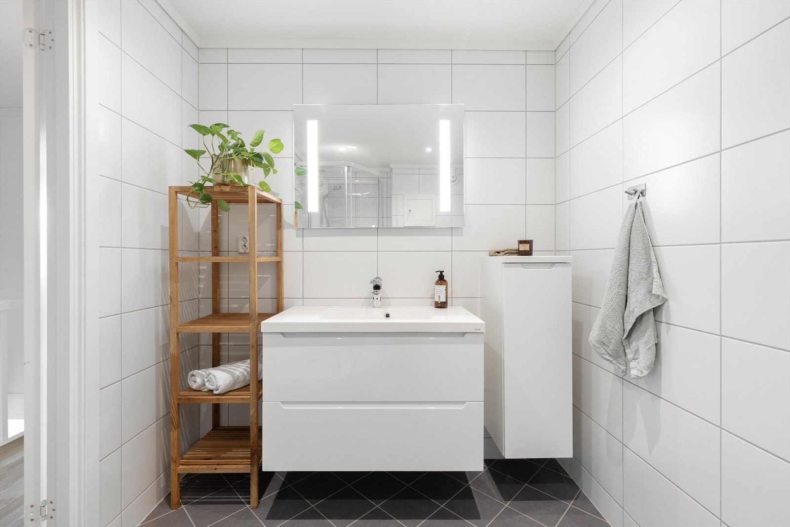 Lekkert baderom fra 2018, utført i regi av borettslaget. Badet er helfliset med varmekabler i gulvet og har en moderne innredning med slette fronter, nedfelt servant og speil med integrert belysning. Galleribilde