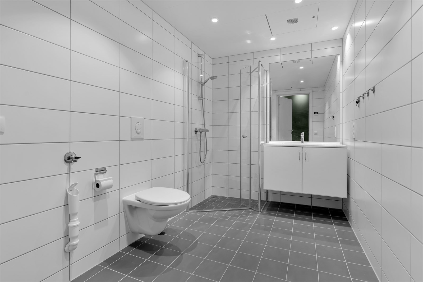 Badet er innredet med vegghengt toalett, baderomsinnredning med servant, dusjdører og garnityr. Opplegg for vaskemaskin Galleribilde