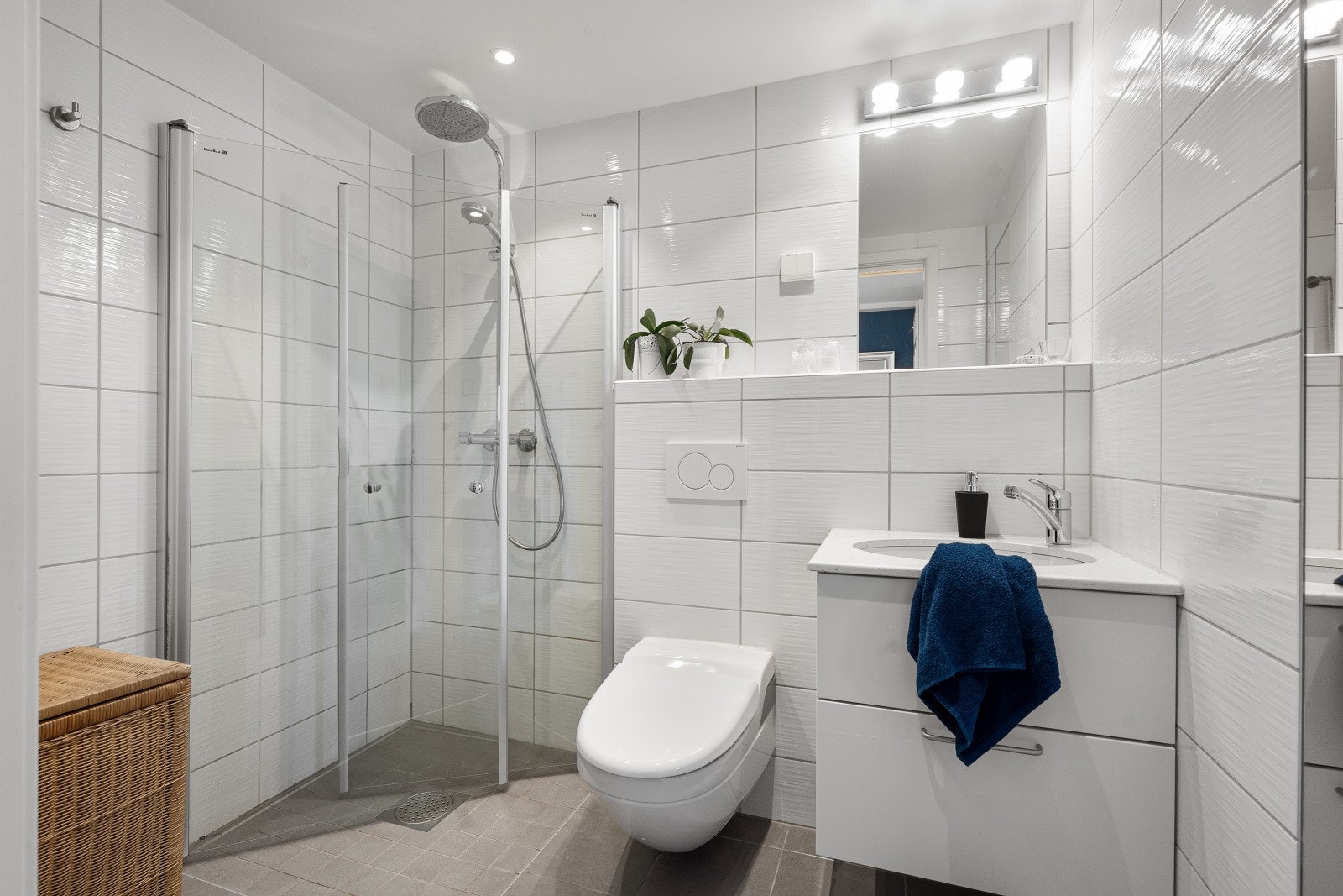 Badet har direkte tilgang fra hovedsoverommet og fremstår moderne med lyse fliser, stilrene detaljer, vegghengt dusjtoalett og romslig dusjnisje med glassvegg. Galleribilde
