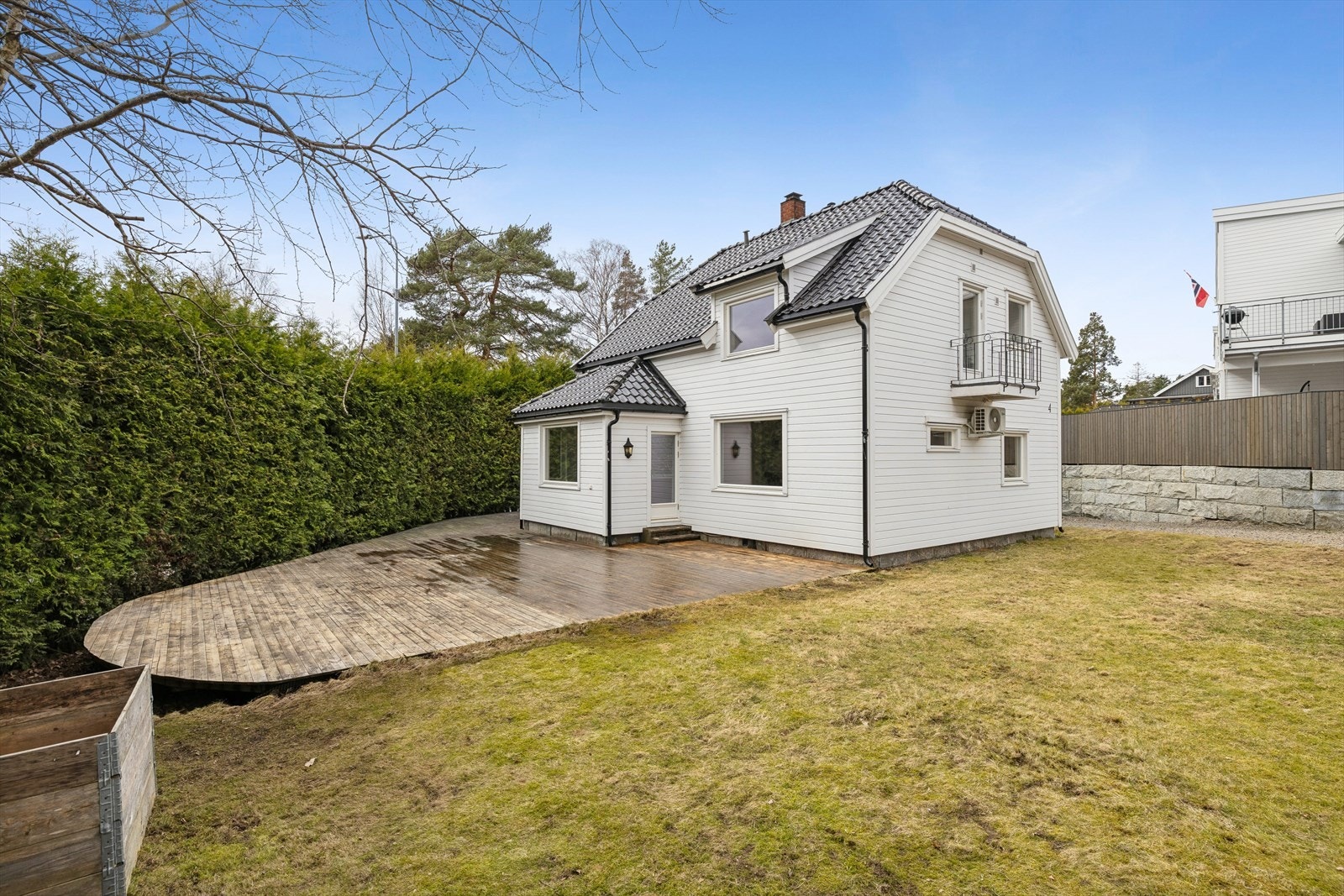 Stor hage og et sammenhengende terrasseområde som strekker seg rundt deler av huset. Galleribilde