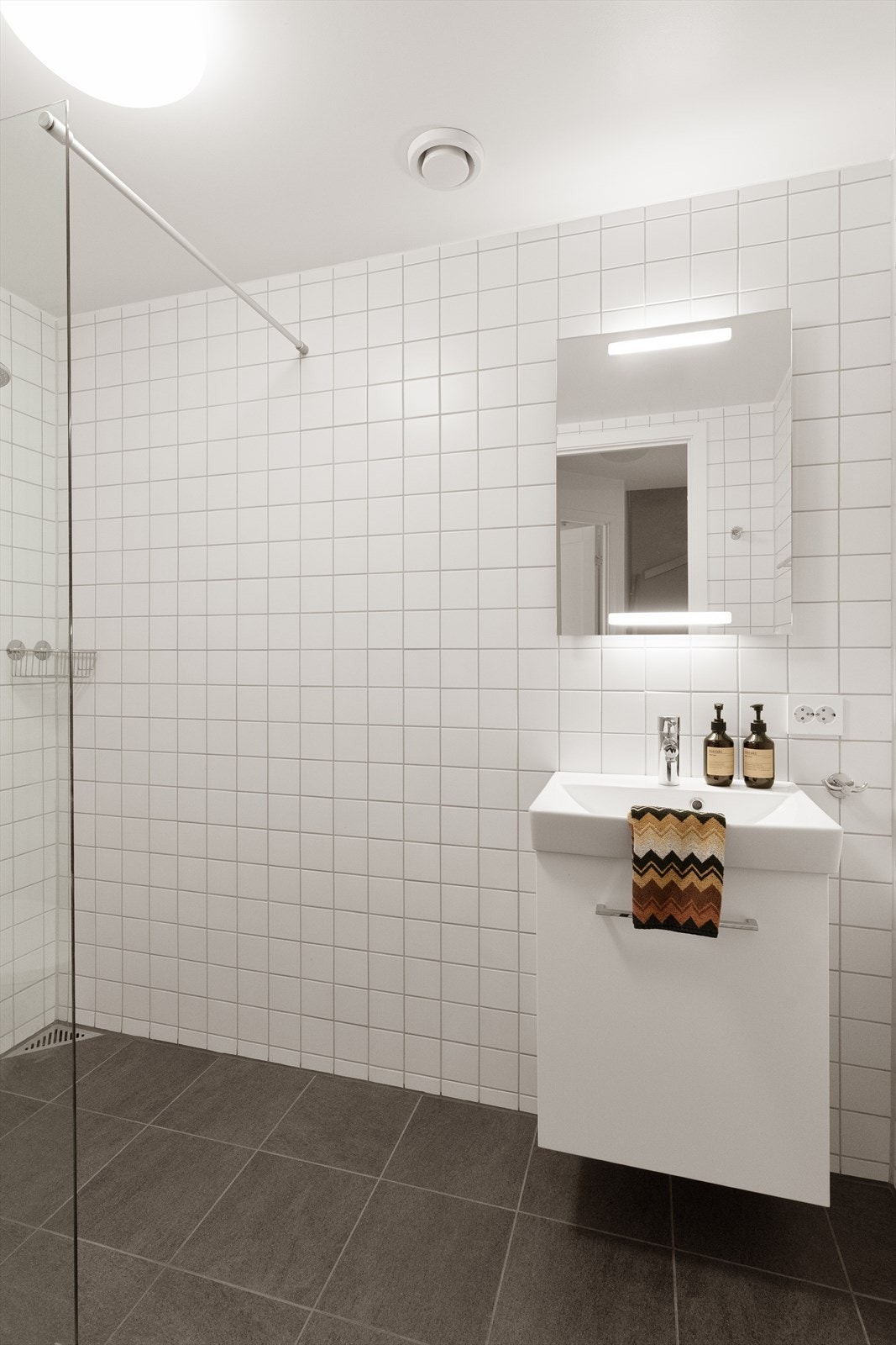 Badet har fliser på gulv og vegger, ellers er det seksjon med hel servant, vegghengt toalett og dusj. Galleribilde