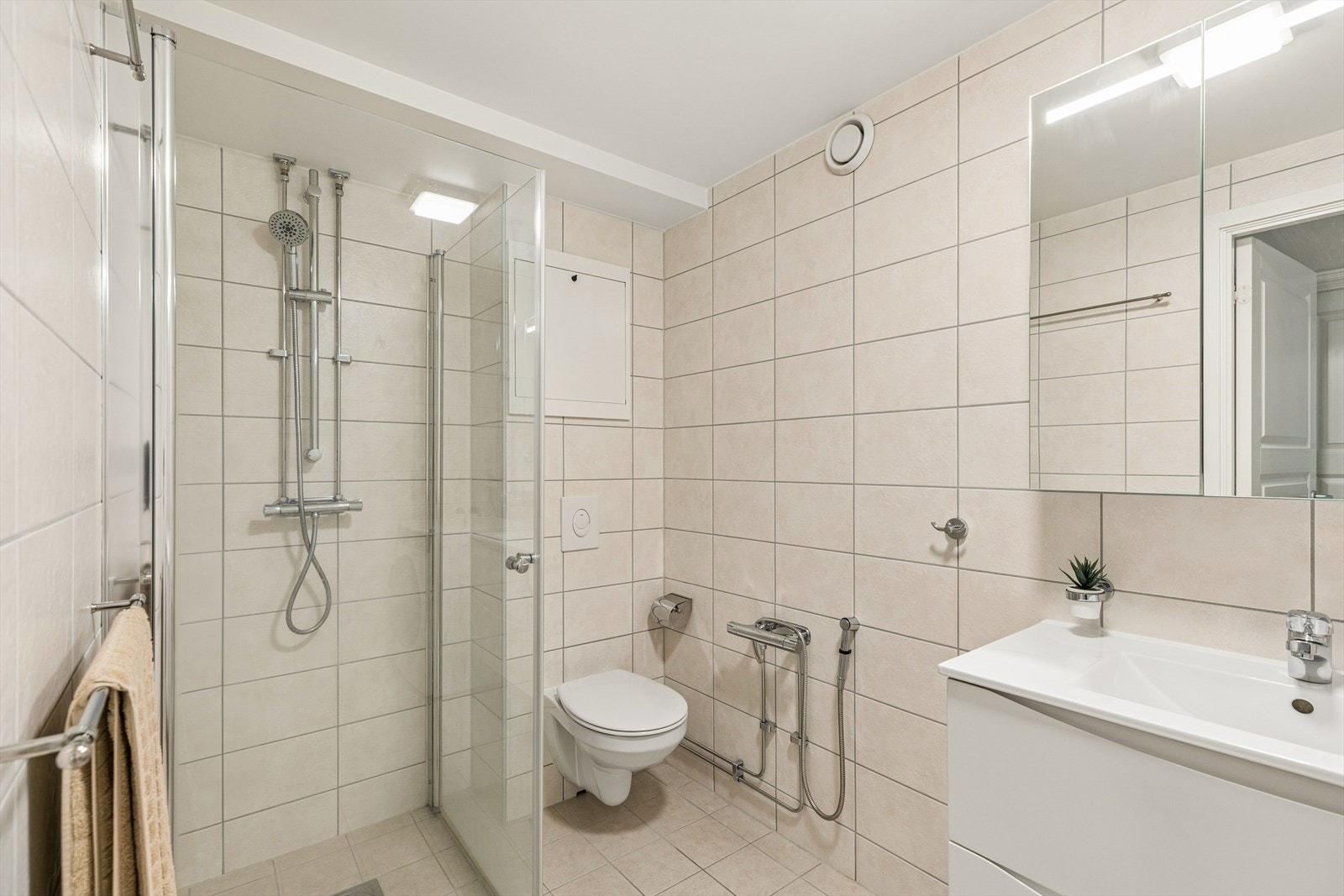 Badet har elektriske varmekabler i det flislagte gulvet, vegghengt toalett og dusjhjørne med innfellbare dører. Galleribilde