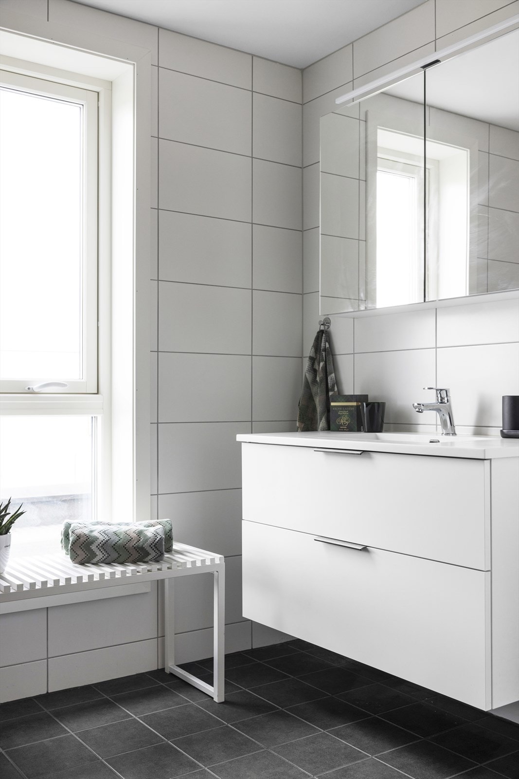 Badet er innredet med vegghengt toalett, dusjhjørne med innfellbare glassdører og baderomsinnredning med skuffer, servant og vegghengt speilskap. Galleribilde