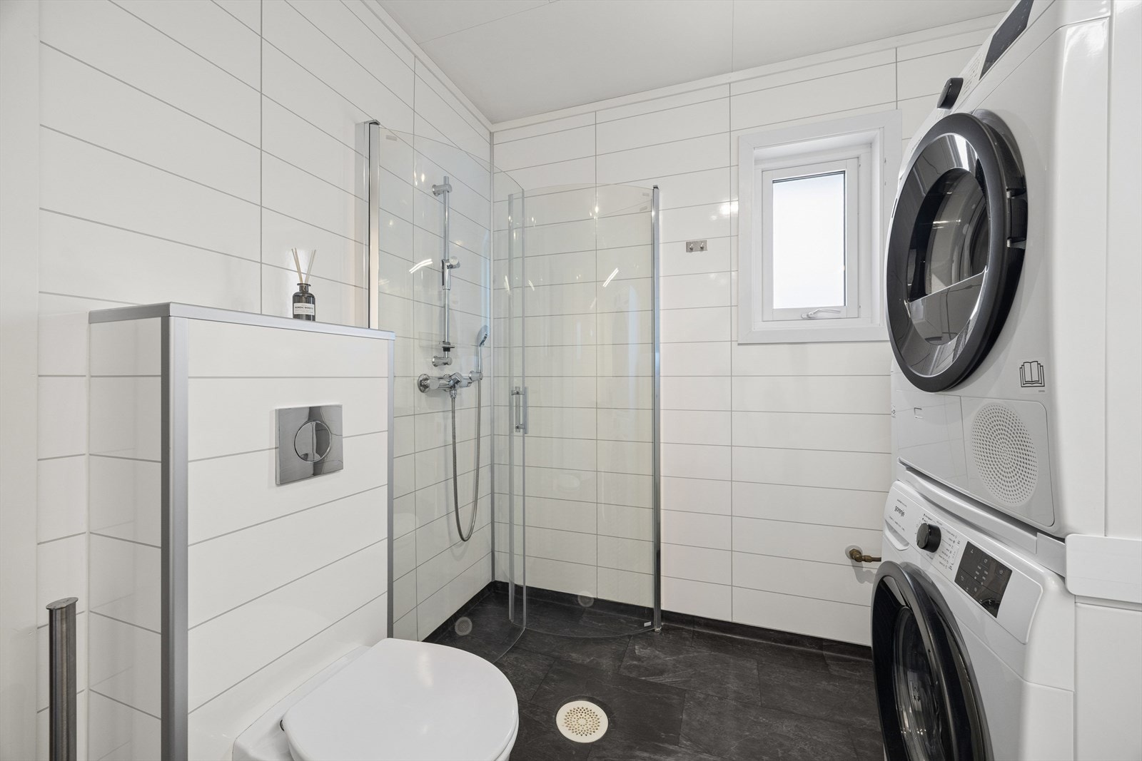 Badet er utstyrt med veggmontert toalett, dusjvegger og har opplegg for vaskemaskin. Galleribilde