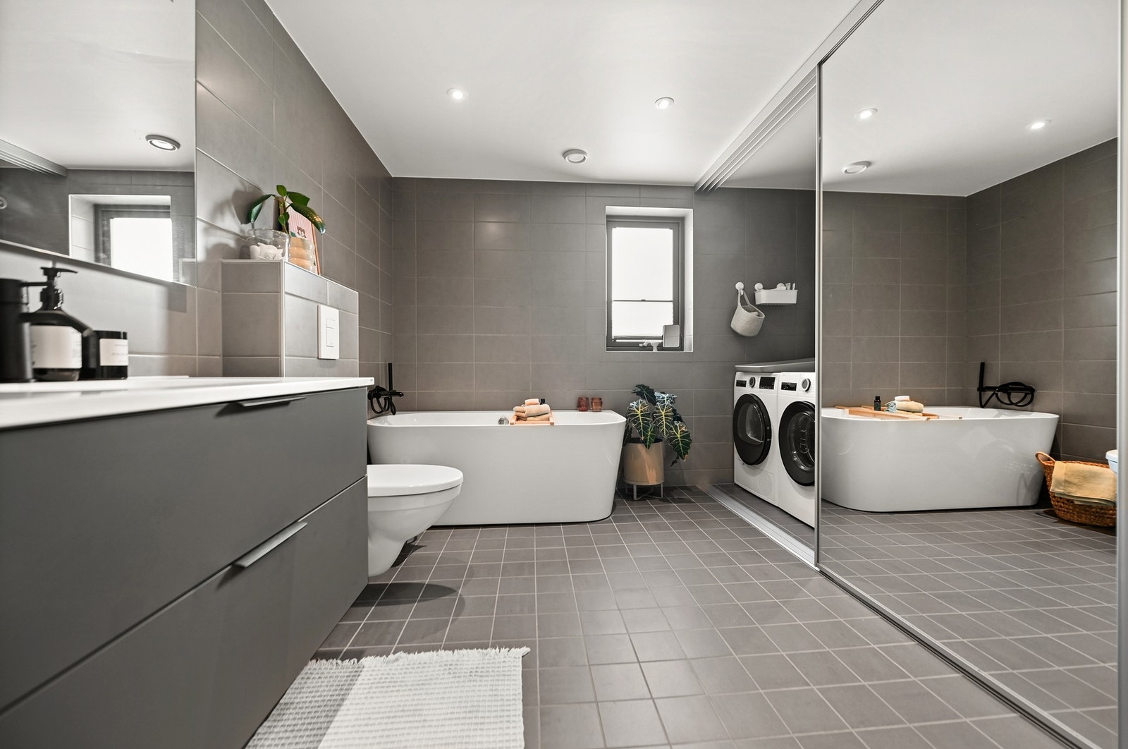 Badet i 1.etg er innredet med nedfelt servant, veggmontert toalett, badekar og egen vaskerom-sone bak skyvedører. Galleribilde