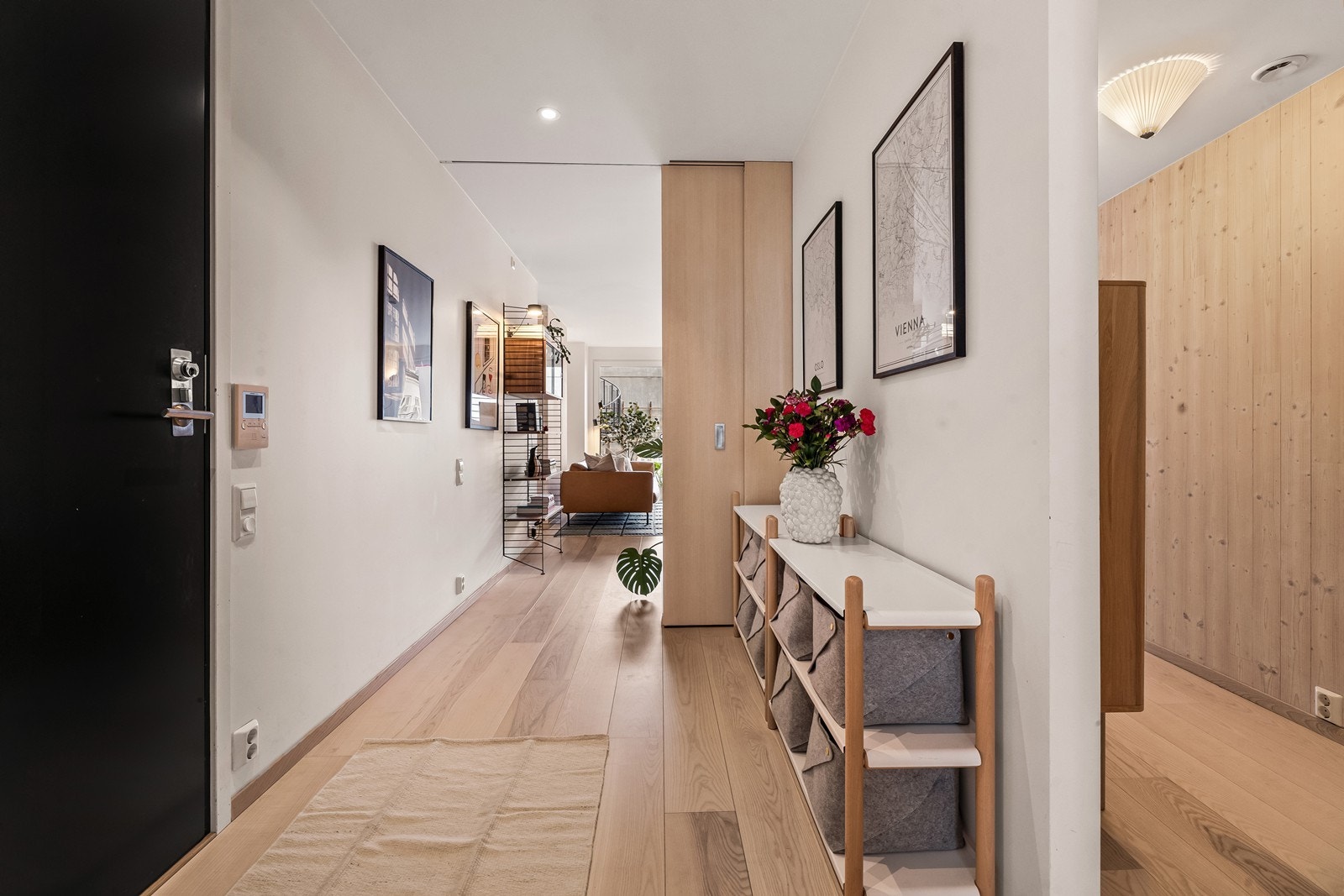Innbydende entré med 1-stavs askeparkett som er gjennomgående i leiligheten. Legge merke til skyvedøren i tre og de gjennomgående tre detaljene i boligen. Galleribilde