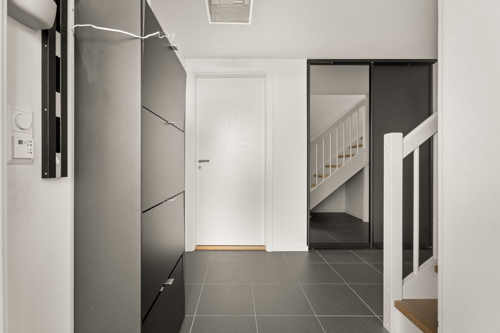 Entréen har slitesterke fliser på gulvet og plass til garderobeløsninger. Trappen med eiketrinn leder opp til hovedetasjen. Galleribilde