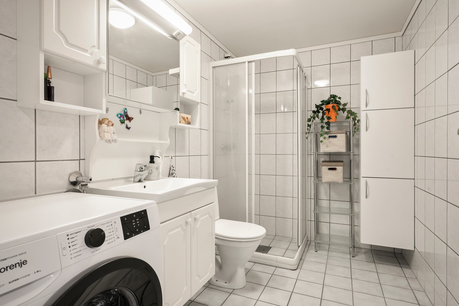 Badet er innredet med servantinnredning med profilerte, lyse fronter, overhengende speil, belysning samt sideskap. Galleribilde