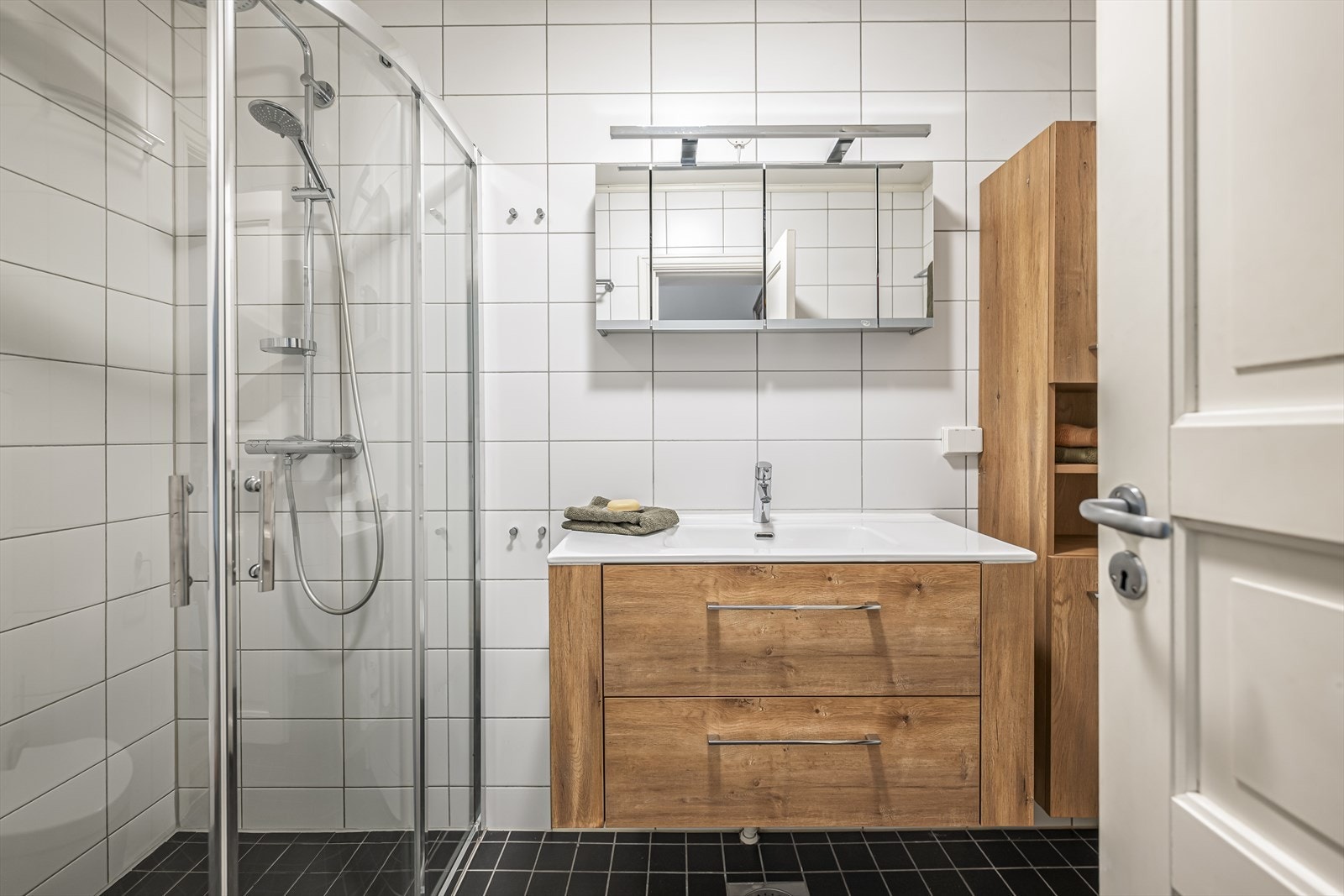 Romslig bad med servantskap, dusjhjørne, høyskap og opplegg for vaskemaskin. Galleribilde
