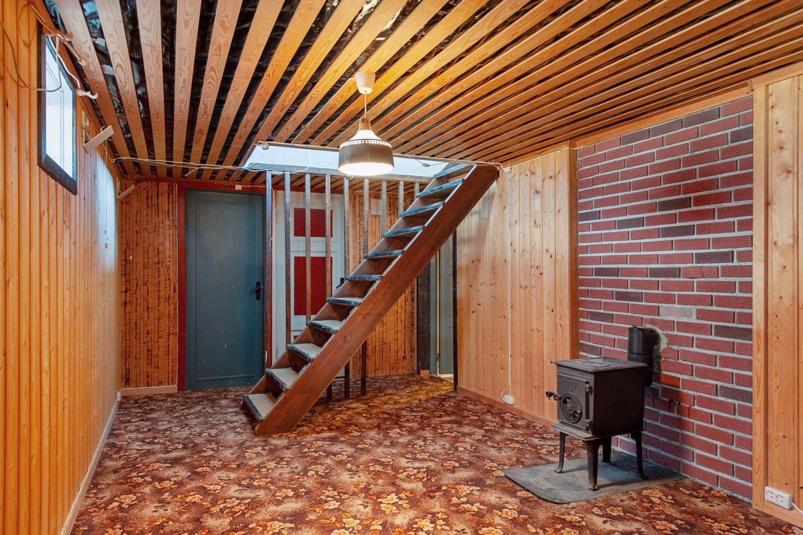 Det innredede rommet i kjelleren har en vedovn og trapp opp til hovedetasjen. Kjelleren inneholder også verksted og tre boder. Galleribilde