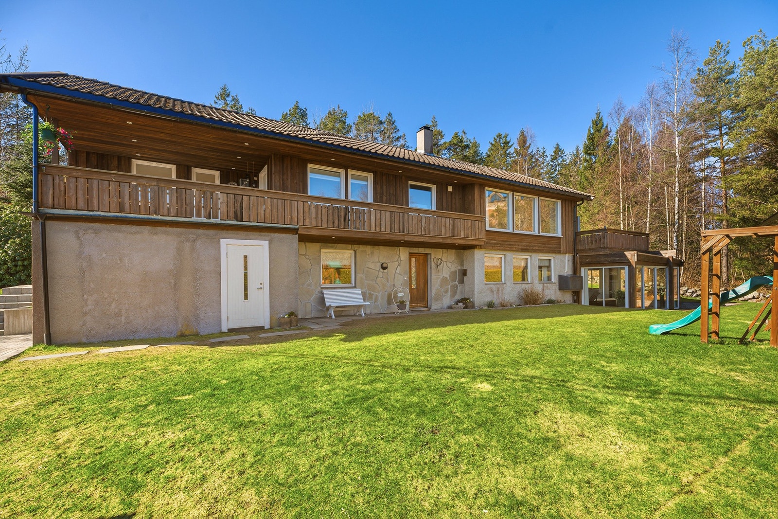Bilde av boligens fasade og hageområde, med gode oppholdsarealer og praktisk utgang til plen fra underetasjen. Galleribilde
