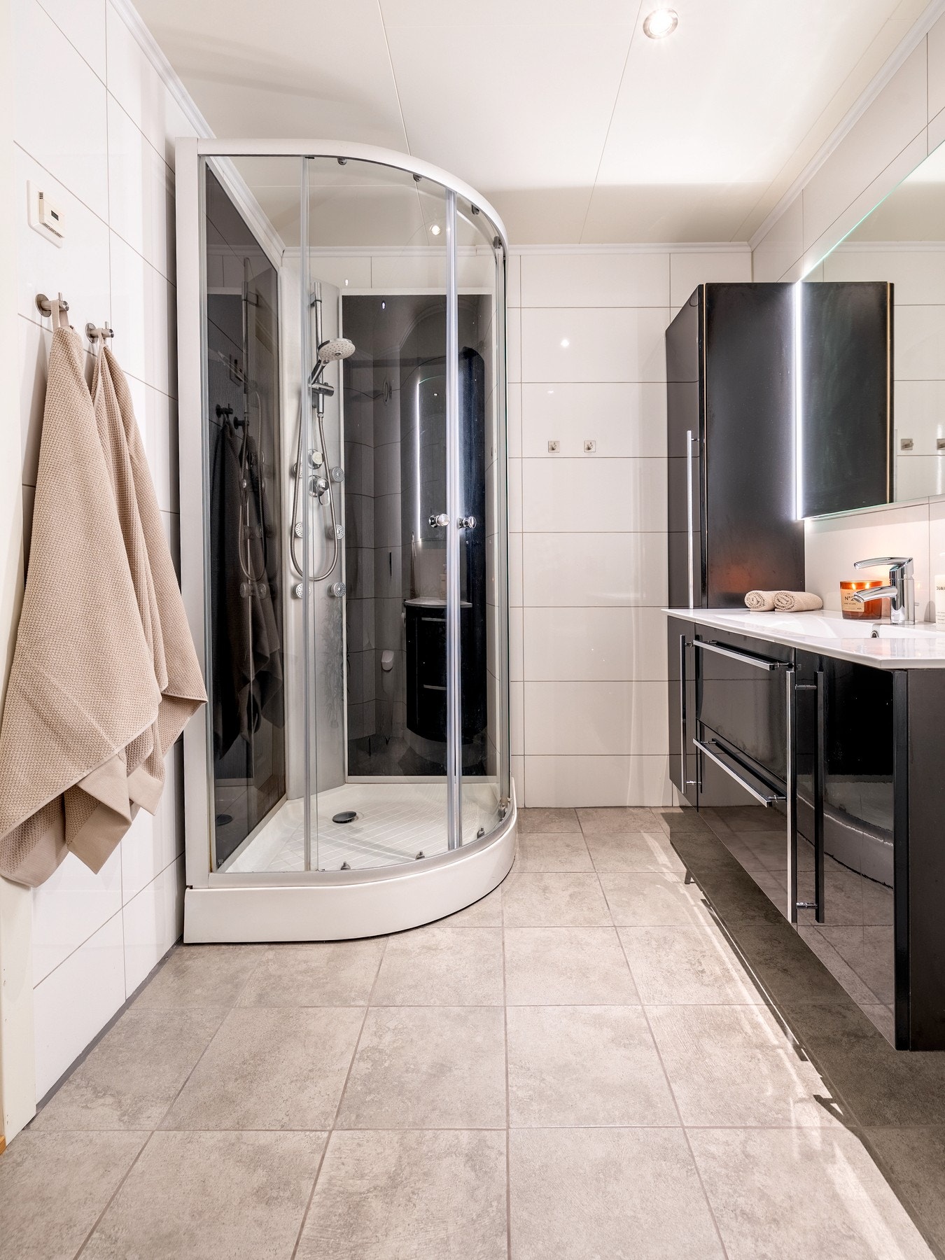 Badet er utstyrt med flislagte vegger og- gulv, elektriske varmekabler og innfelt downlights. Innredningen består av nedfelt servant på skap- og skuffeseksjon, ett høyskap, speil med belysning, veggmontert toalett og dusjkabinett. Galleribilde
