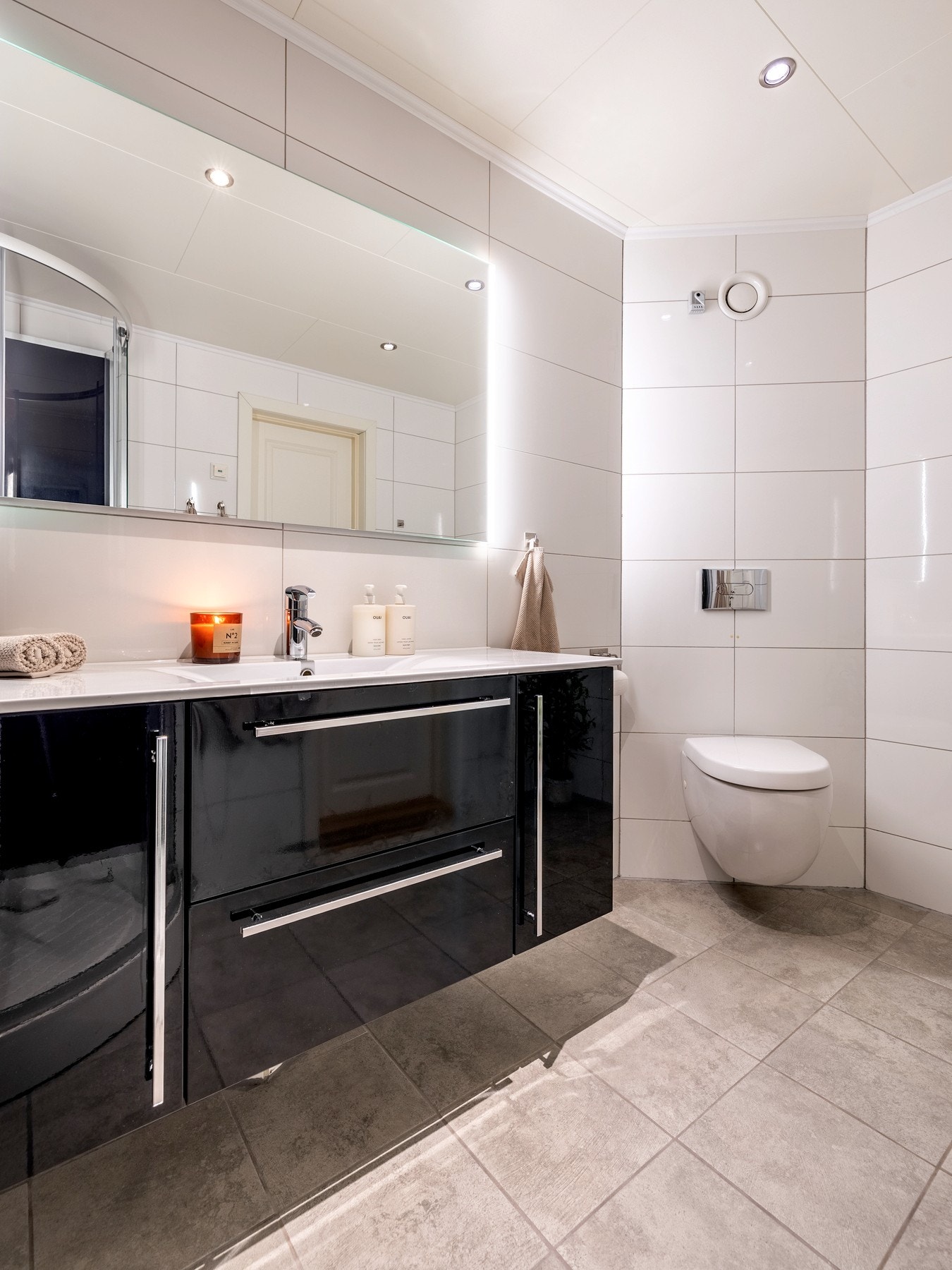 Badet er utstyrt med flislagte vegger og- gulv, elektriske varmekabler og innfelt downlights. Innredningen består av nedfelt servant på skap- og skuffeseksjon, ett høyskap, speil med belysning, veggmontert toalett og dusjkabinett. Galleribilde