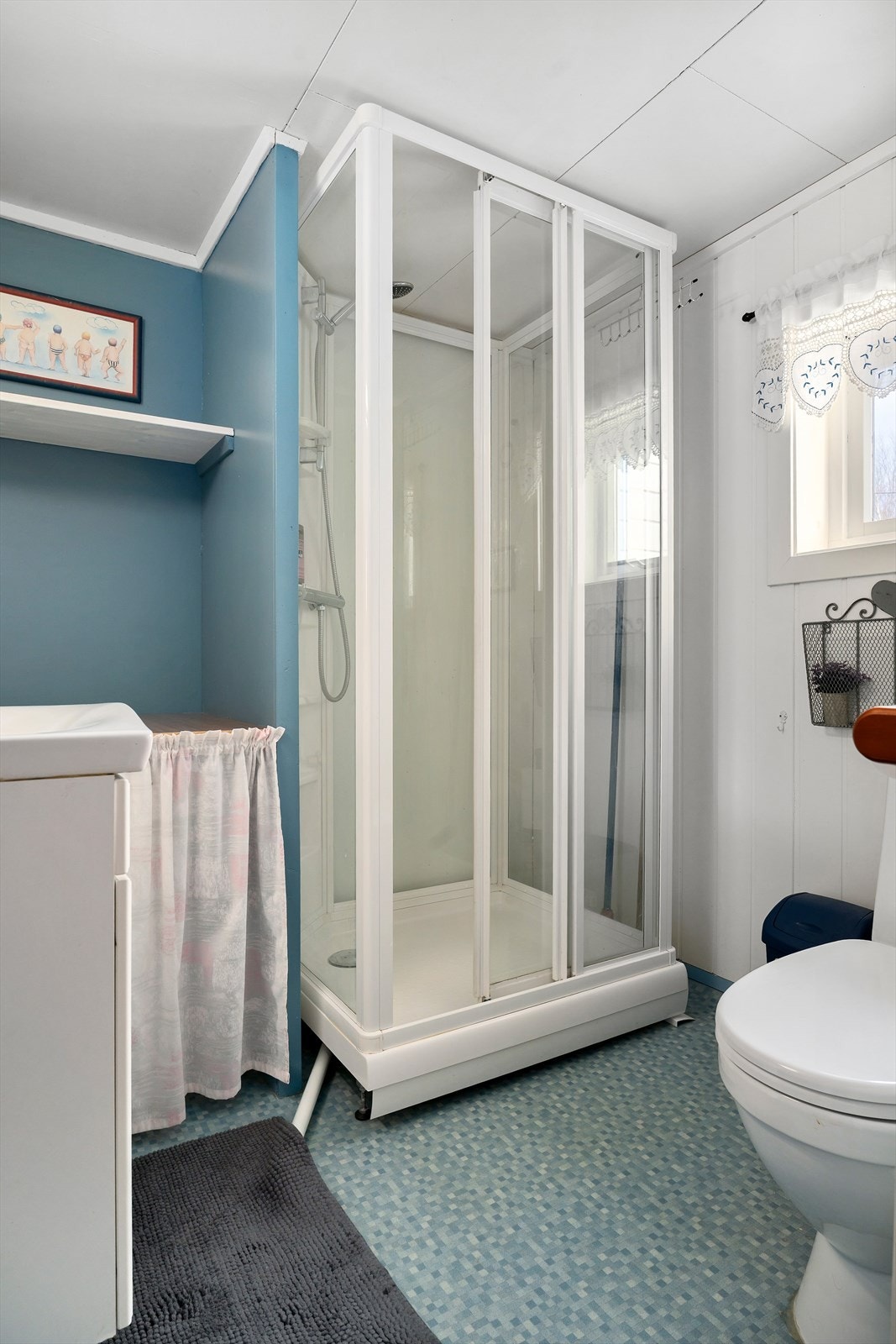 Bad i første etasje: Badet har vinylbelegg på gulvet, malte plater på veggene og malte plater i himlingen. Rommet er utstyrt med dusjkabinett, gulvmontert toalett og en
innredning med servant med ett-greps blandebatteri. Galleribilde