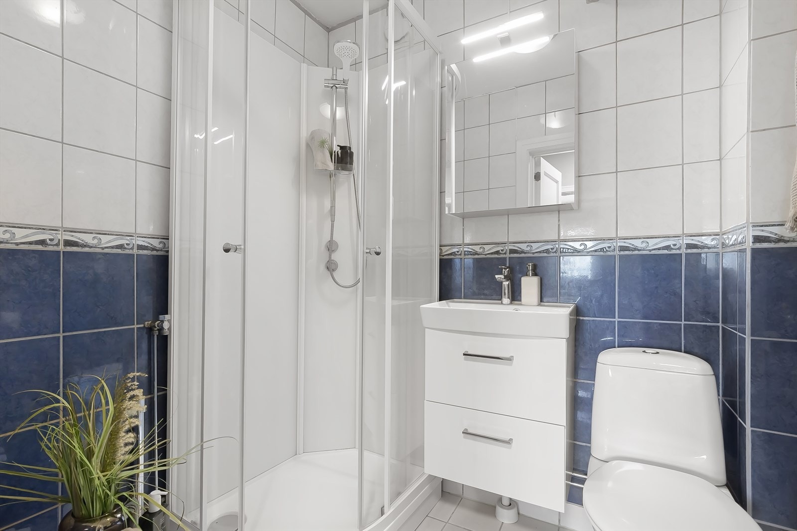 Pent og romslig bad med servantinnredning, toalett og dusjkabinett. Badet fremstår lyst og innbydende med flislagte vegger. Galleribilde