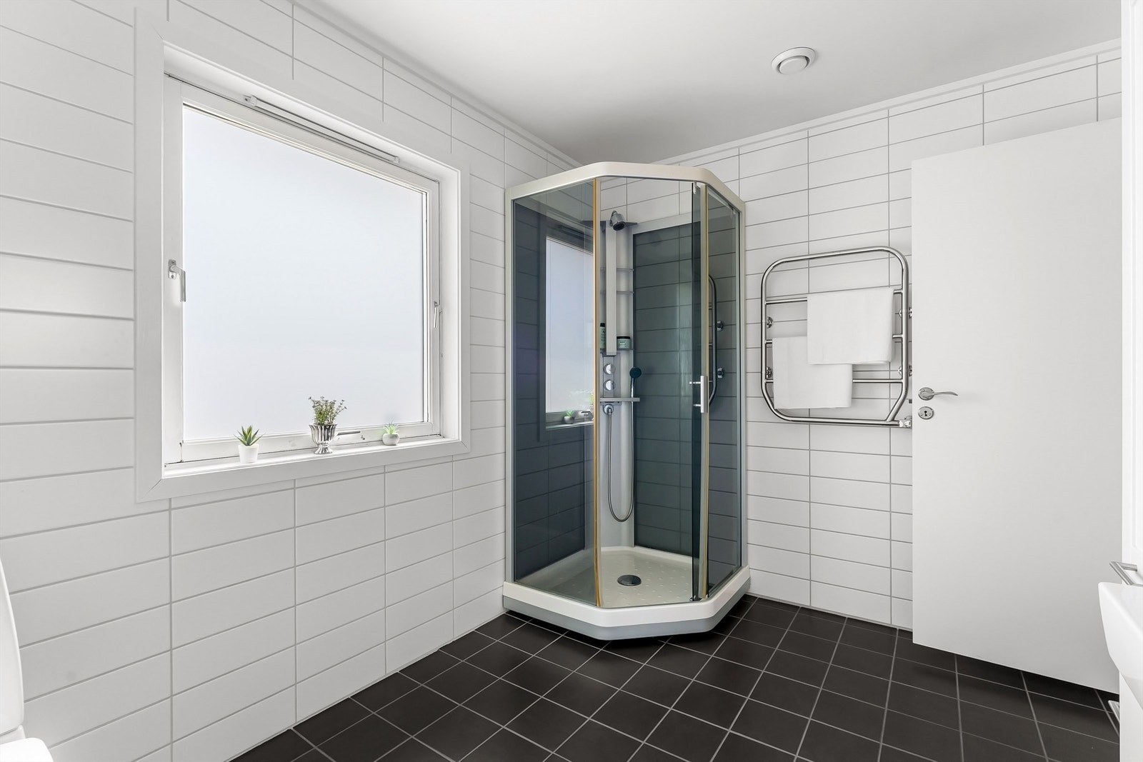 Badet har toalett, vegghengt servantinnredning med ovenpåliggende servant, speilskap med overlys over servant, vegghengt skap og dusjkabinett Galleribilde