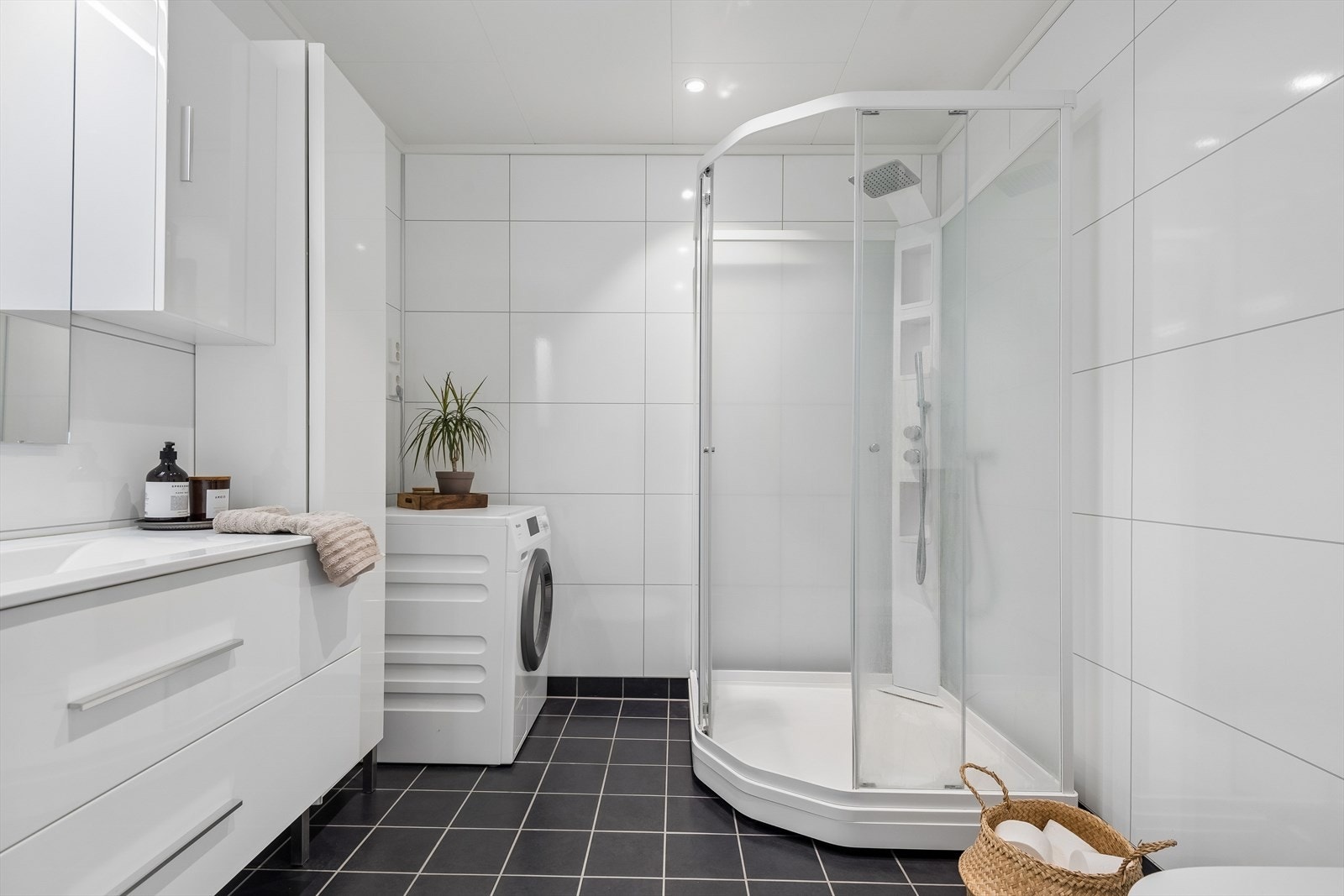 Badet har flislagt gulv med vannbåren gulvvarme og baderomsplater på veggene. Her er det dusjkabinett og opplegg for vaskemaskin. Galleribilde