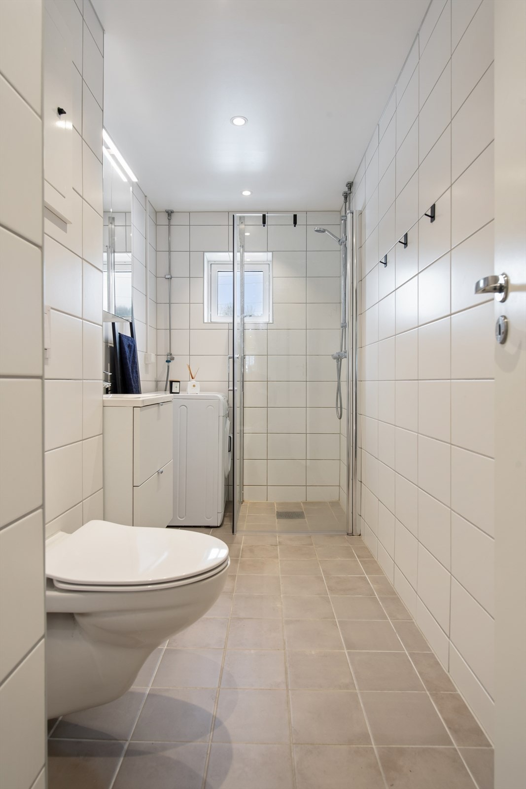 Videre har badet veggmontert toalett og dusjløsning med dusjvegger. Det er også opplegg for vaskemaskin. Galleribilde
