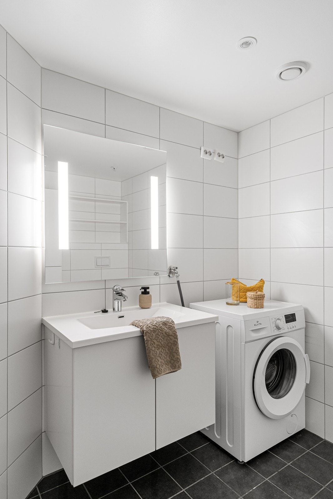 Badet har innredning med nedfelt servant, veggmontert toalett og dusjløsning med vegger/hjørne. Det er også opplegg for vaskemaskin, noe som gir en praktisk og funksjonell løsning. Galleribilde