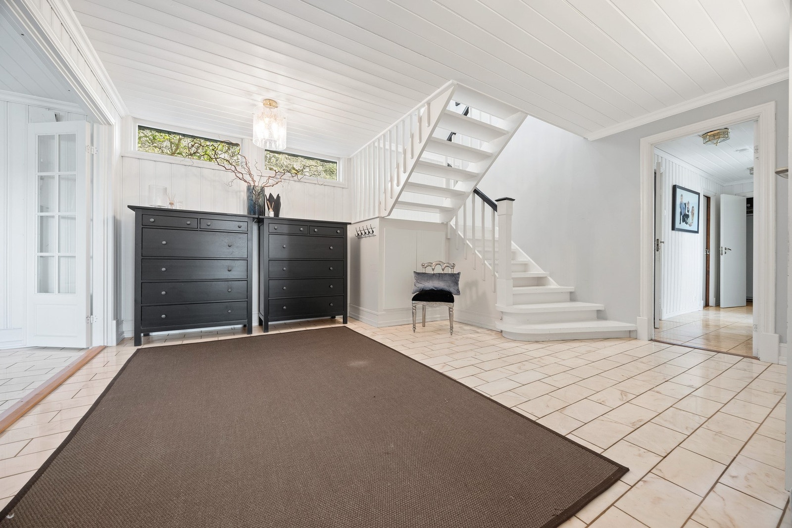 Lyst og romslig inngangsparti med flislagt gulv og trapp til andre etasje Galleribilde