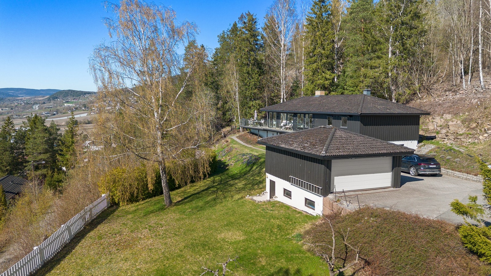 Sort hus med garasje og stor uteplass, grnesende mot marka og med utsikt over dalen. Galleribilde