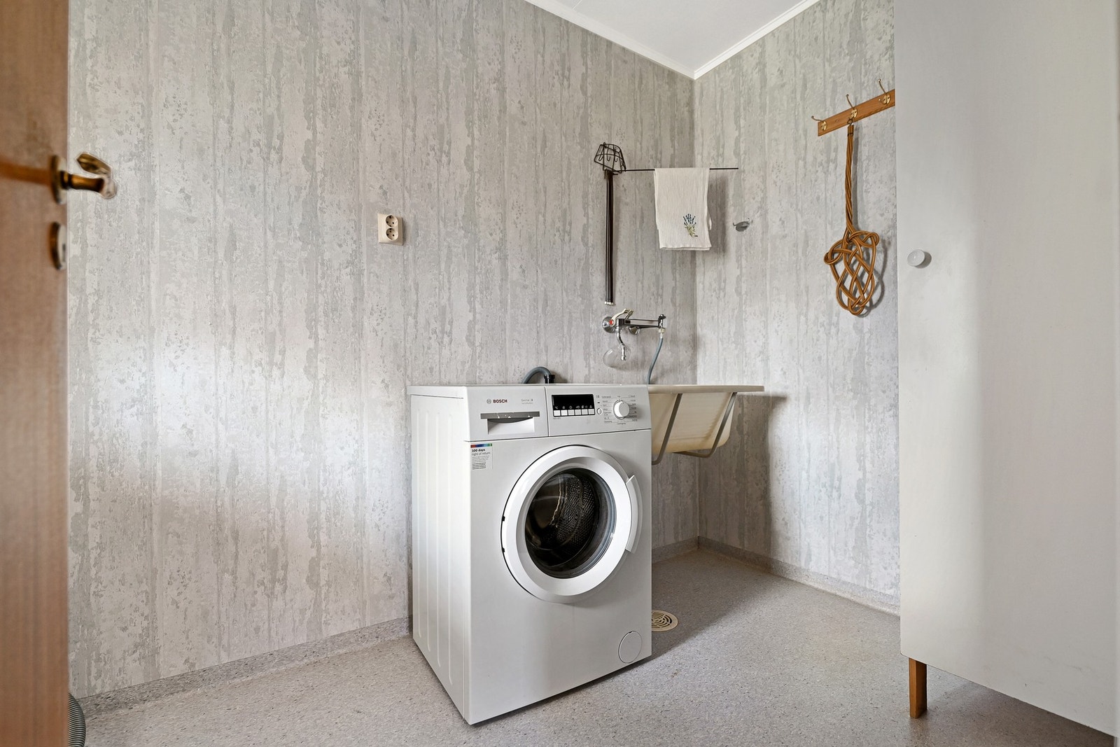 Vaskerom med vaskemaskin og vask, vegghengt tørkestativ og knagger. Galleribilde