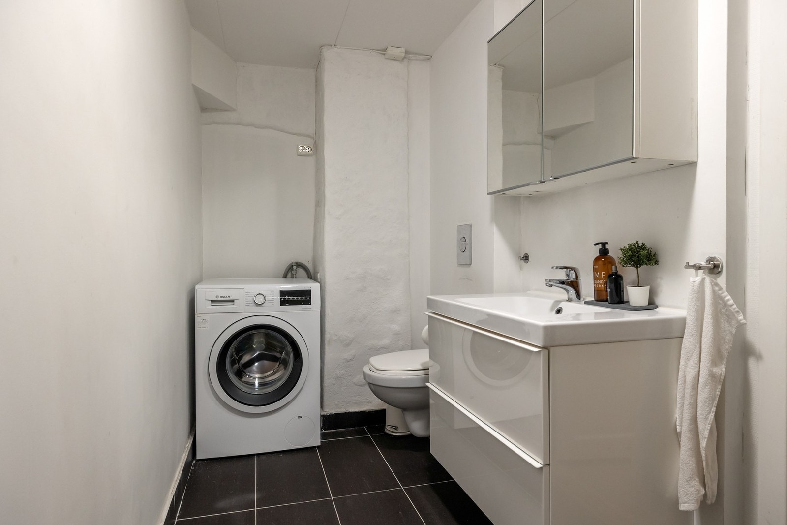 Badet har flislagt gulv, og er innredet med dusjkabinett, vegghengt toalett og servantinnredning med oppbevaring. her er det også opplegg for vaskemaskin. Galleribilde